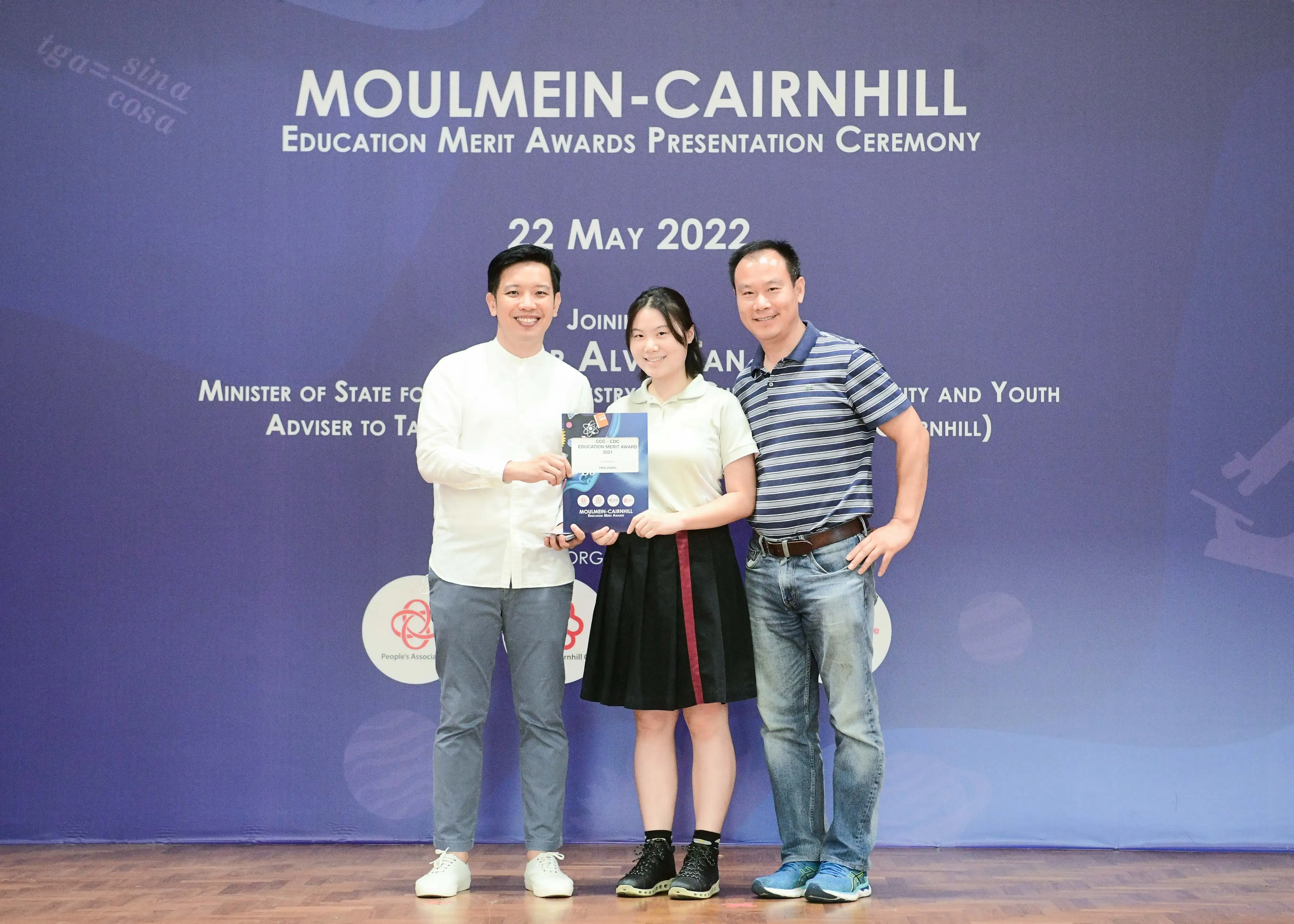 Three people pose with an award certificate at the Moulmein-Cairnhill Education Merit Awards ceremony on 22 May 2022.