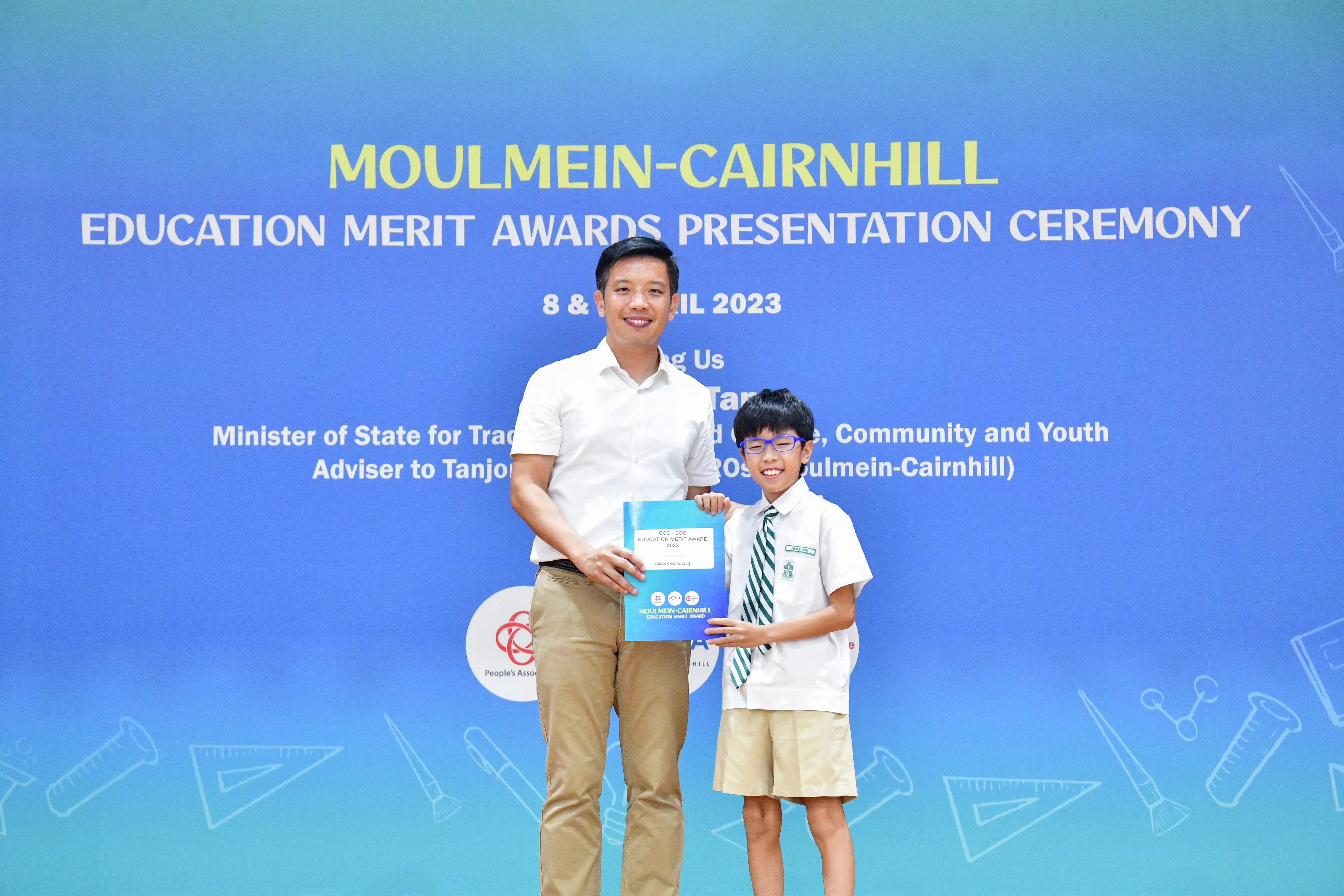 Adult and young student in school uniform hold an award together at Moulmein-Cairnhill Education Merit Awards 2023.