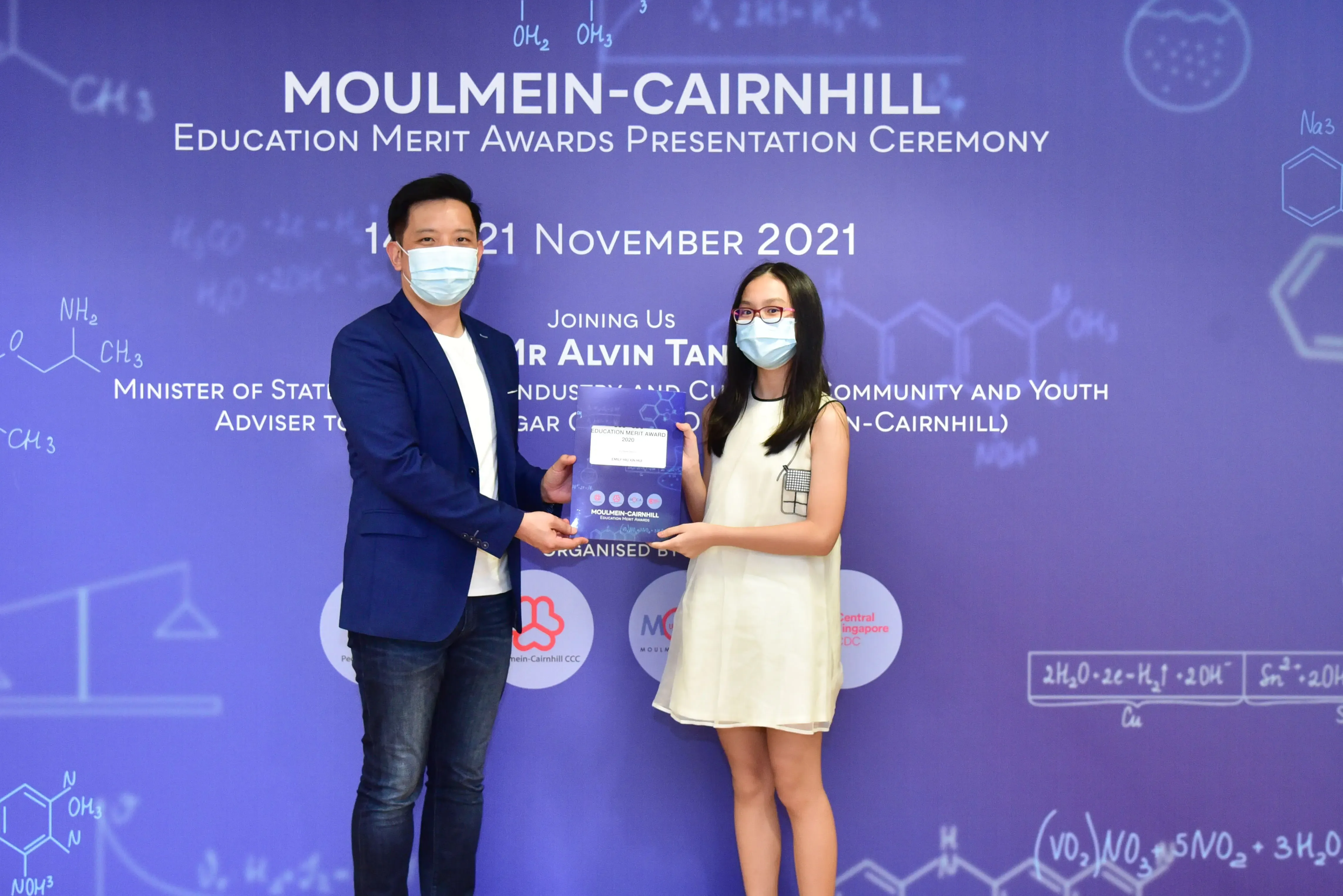 Two masked people hold a certificate at the Moulmein-Cairnhill Education Merit Awards Ceremony, November 2021.
