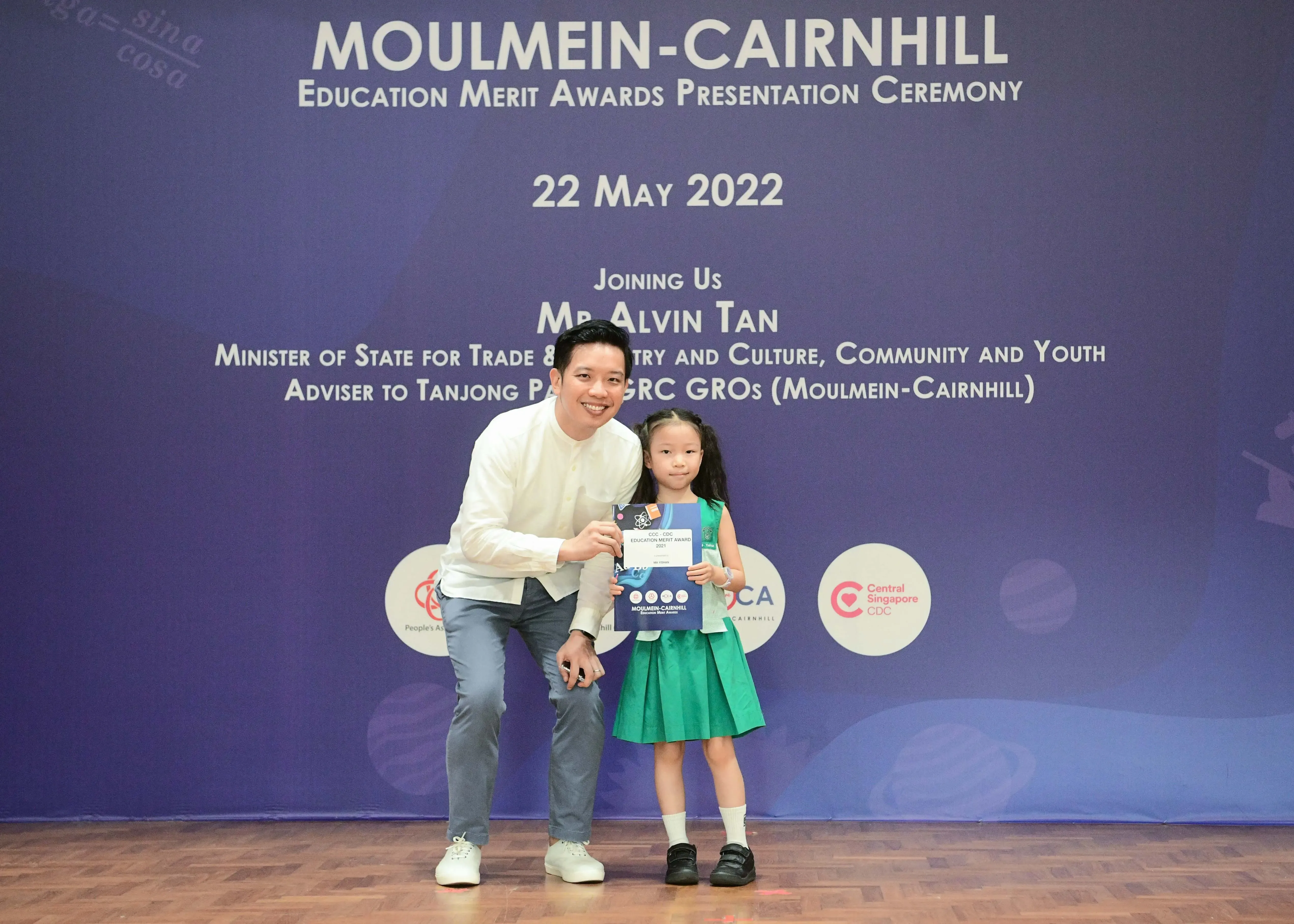 A man and a young girl hold a certificate at the Moulmein-Cairnhill Education Merit Awards Ceremony on 22 May 2022.