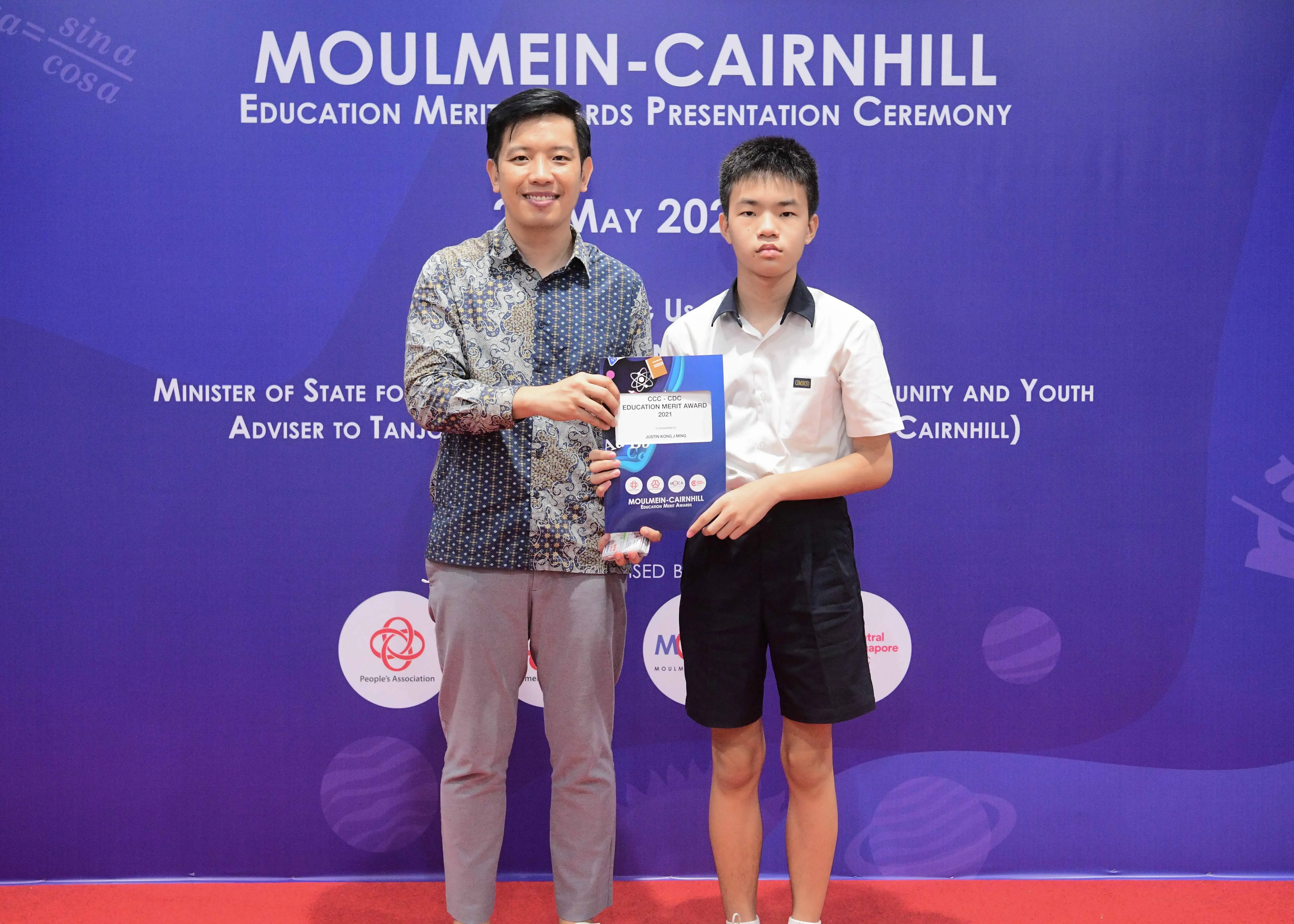 Two people hold an award certificate at the Moulmein-Cairnhill Education Merit Awards Presentation Ceremony.