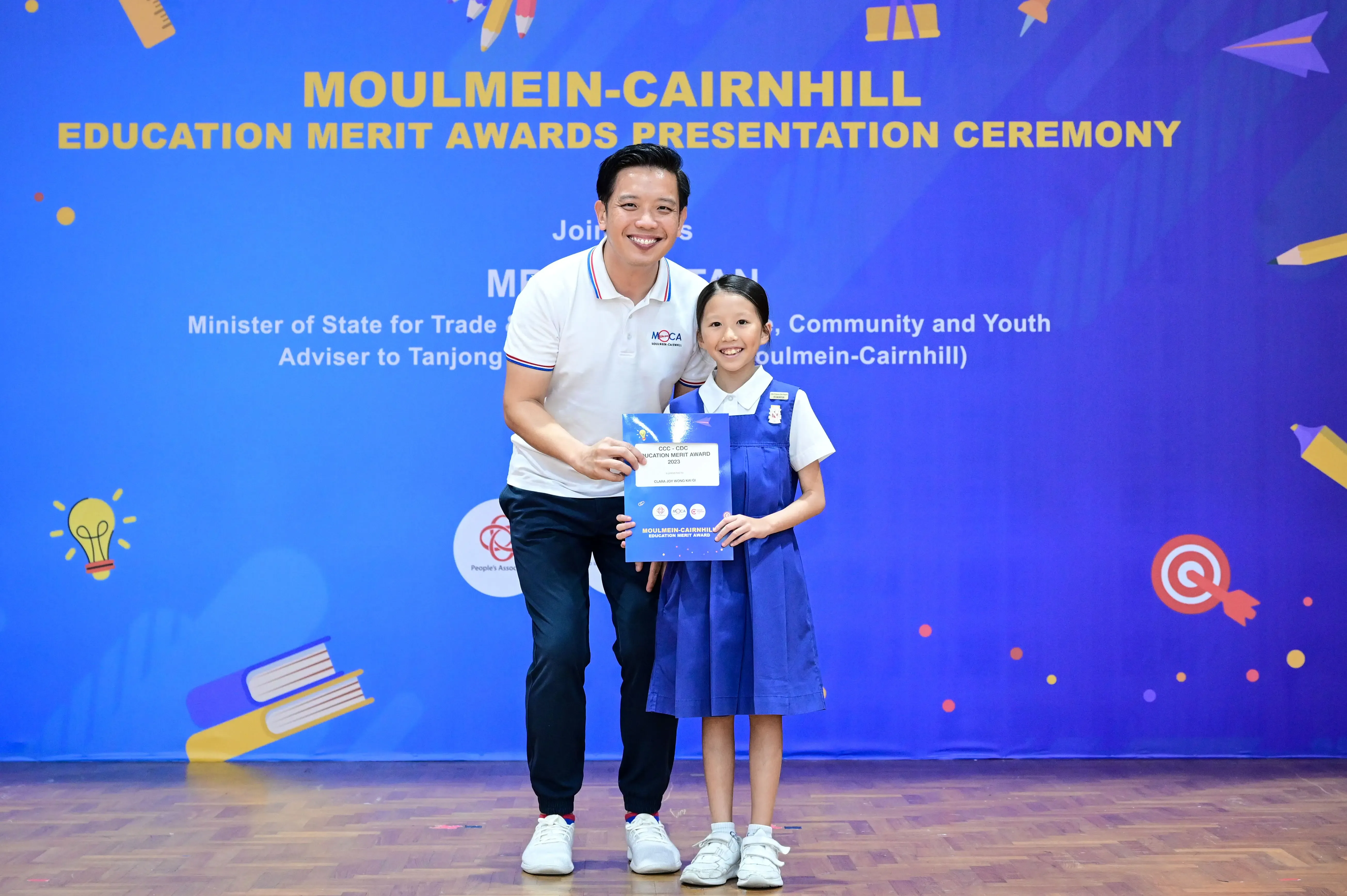 A man and a young girl in school uniform hold an award certificate at the Moulmein-Cairnhill Education Merit Awards ceremony.