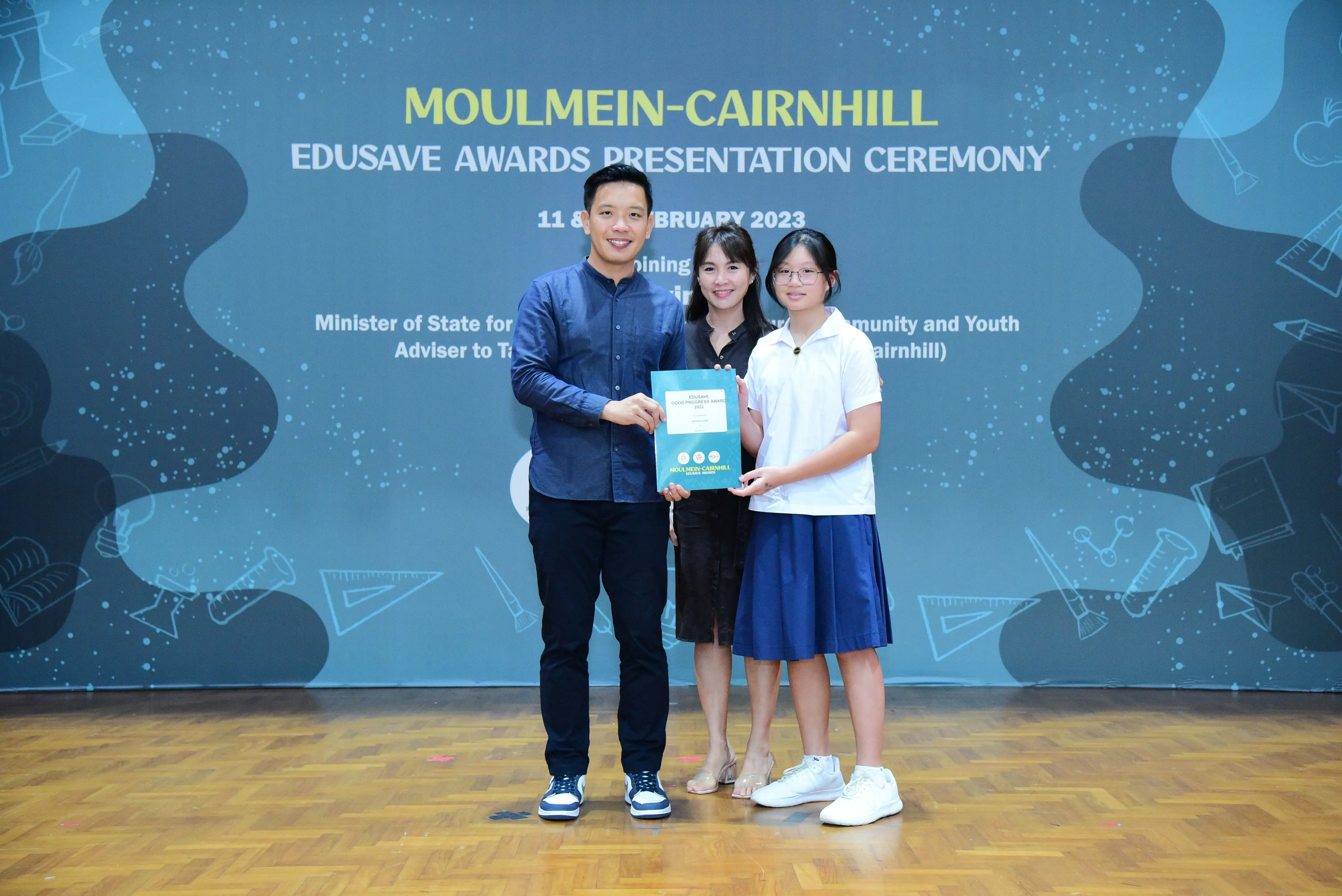 Three people pose holding a certificate at the Moulmein-Cairnhill Edusave Awards Presentation Ceremony 2023.