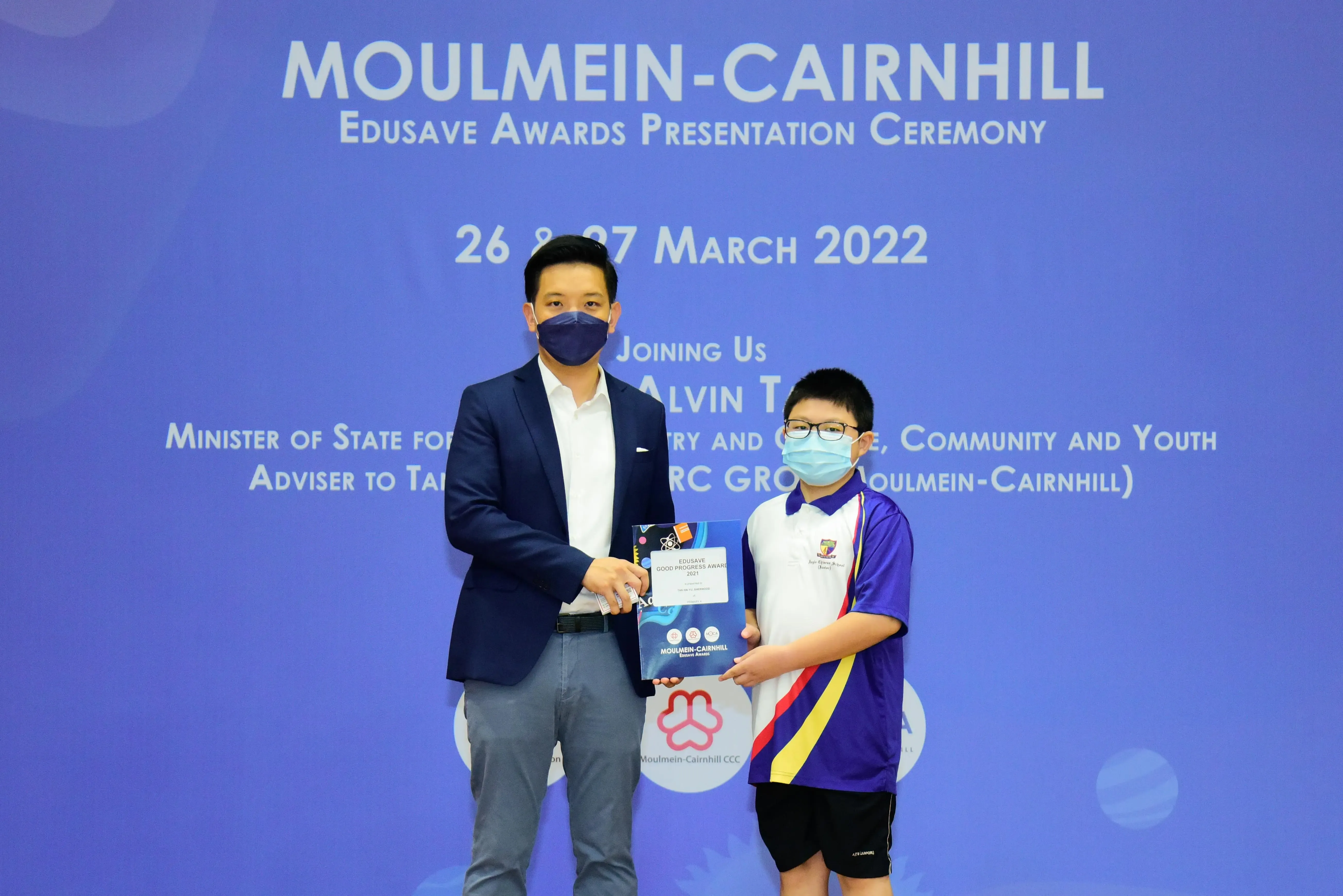 An adult in a suit and a young student in school uniform hold a certificate at the Moulmein-Cairnhill Edusave Awards 2022.