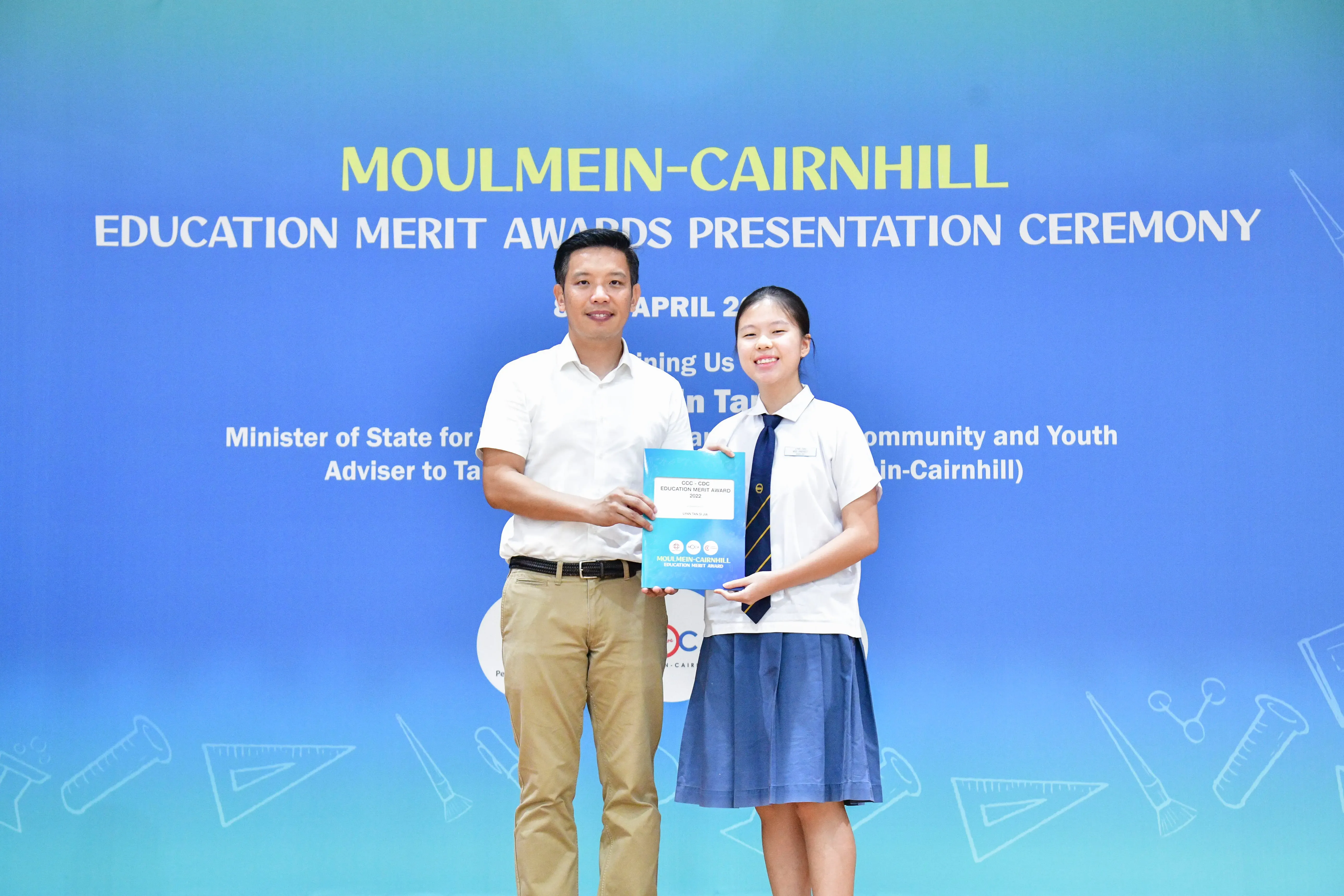 A man and a uniformed student hold an award together at the Moulmein-Cairnhill Education Merit Awards Ceremony.