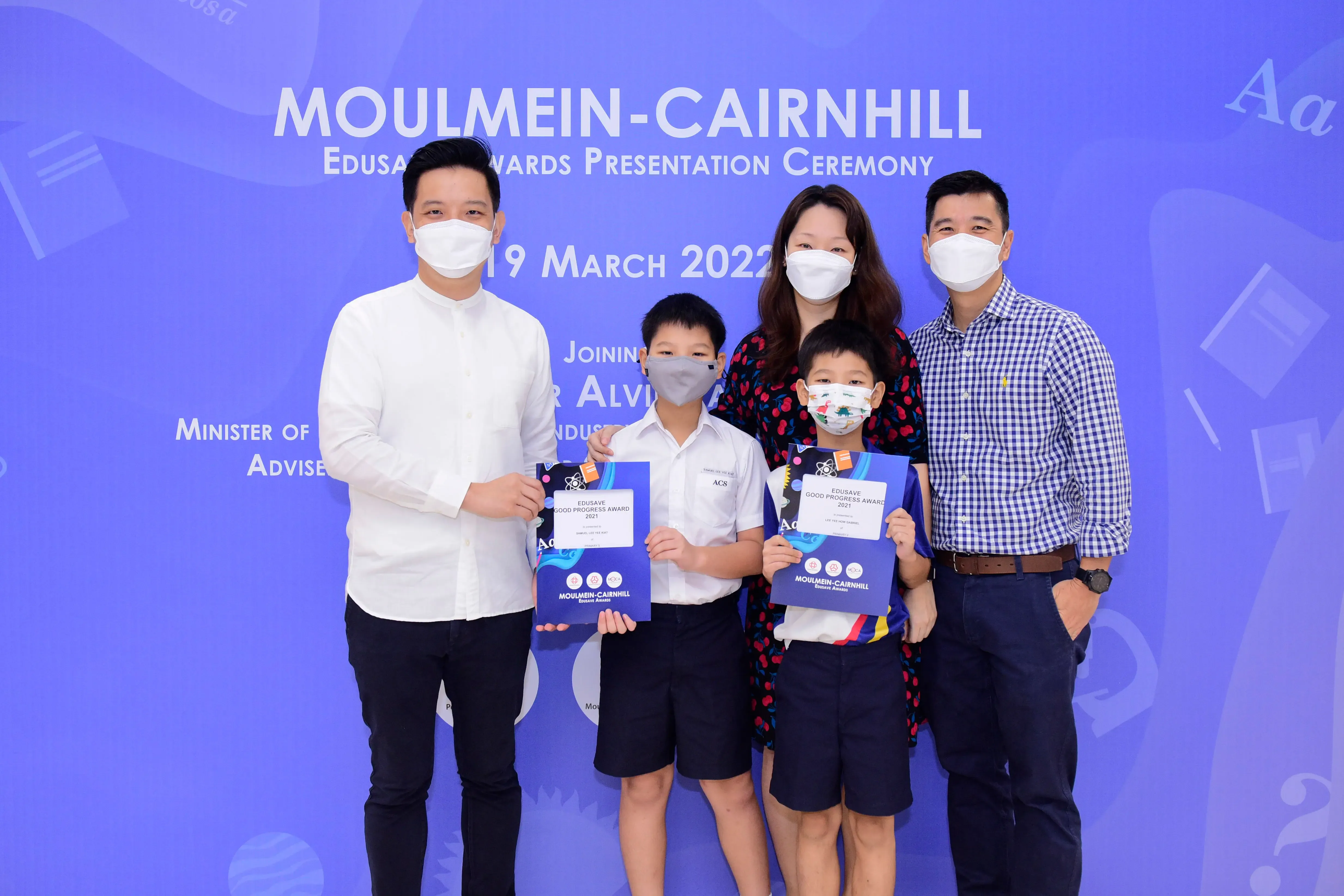 Five masked people pose at the Moulmein-Cairnhill Edusave Awards Ceremony on 19 March 2022, two children holding award certificates.