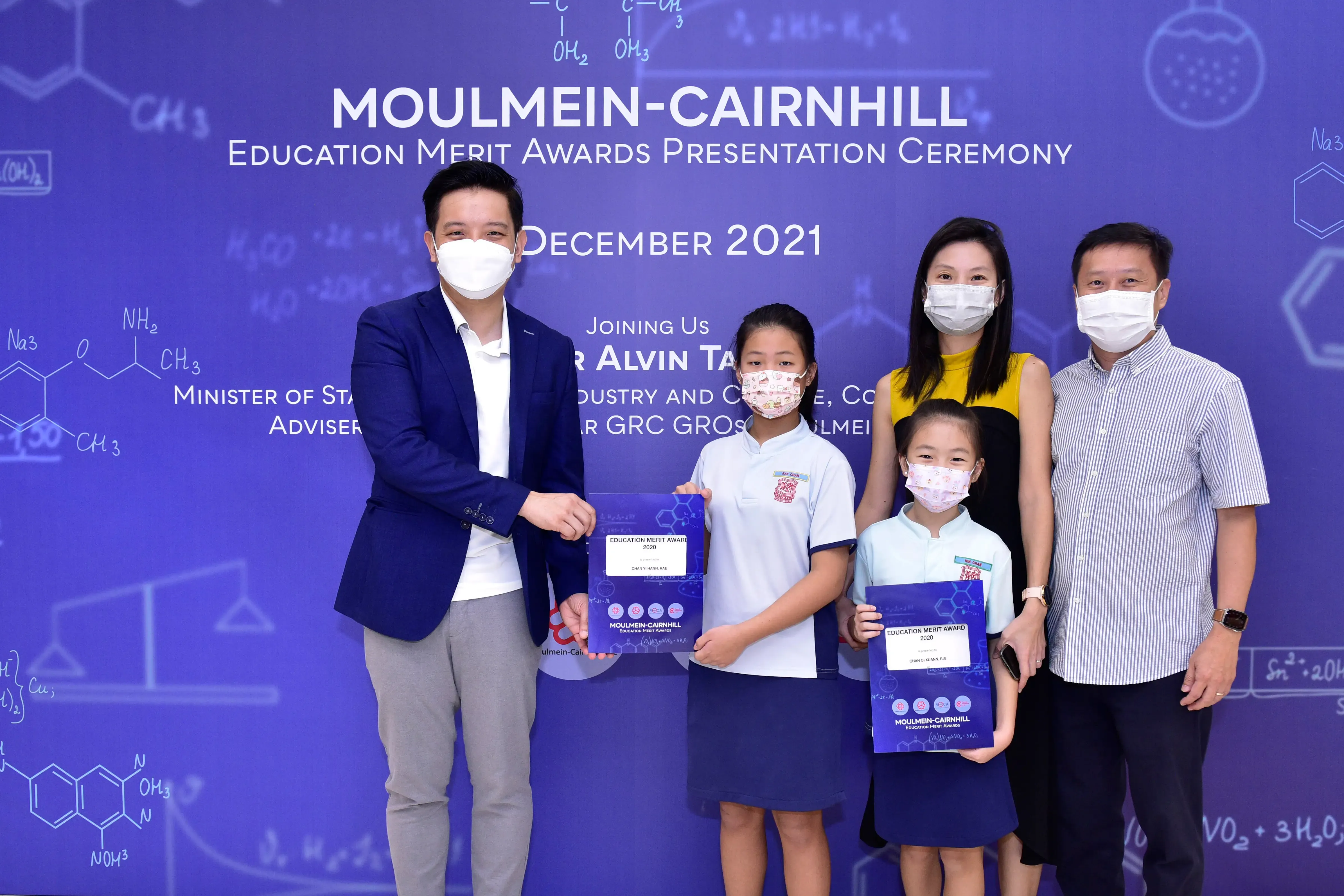 Five masked people pose at the Moulmein-Cairnhill Education Merit Awards Ceremony in December 2021, two girls holding award folders.