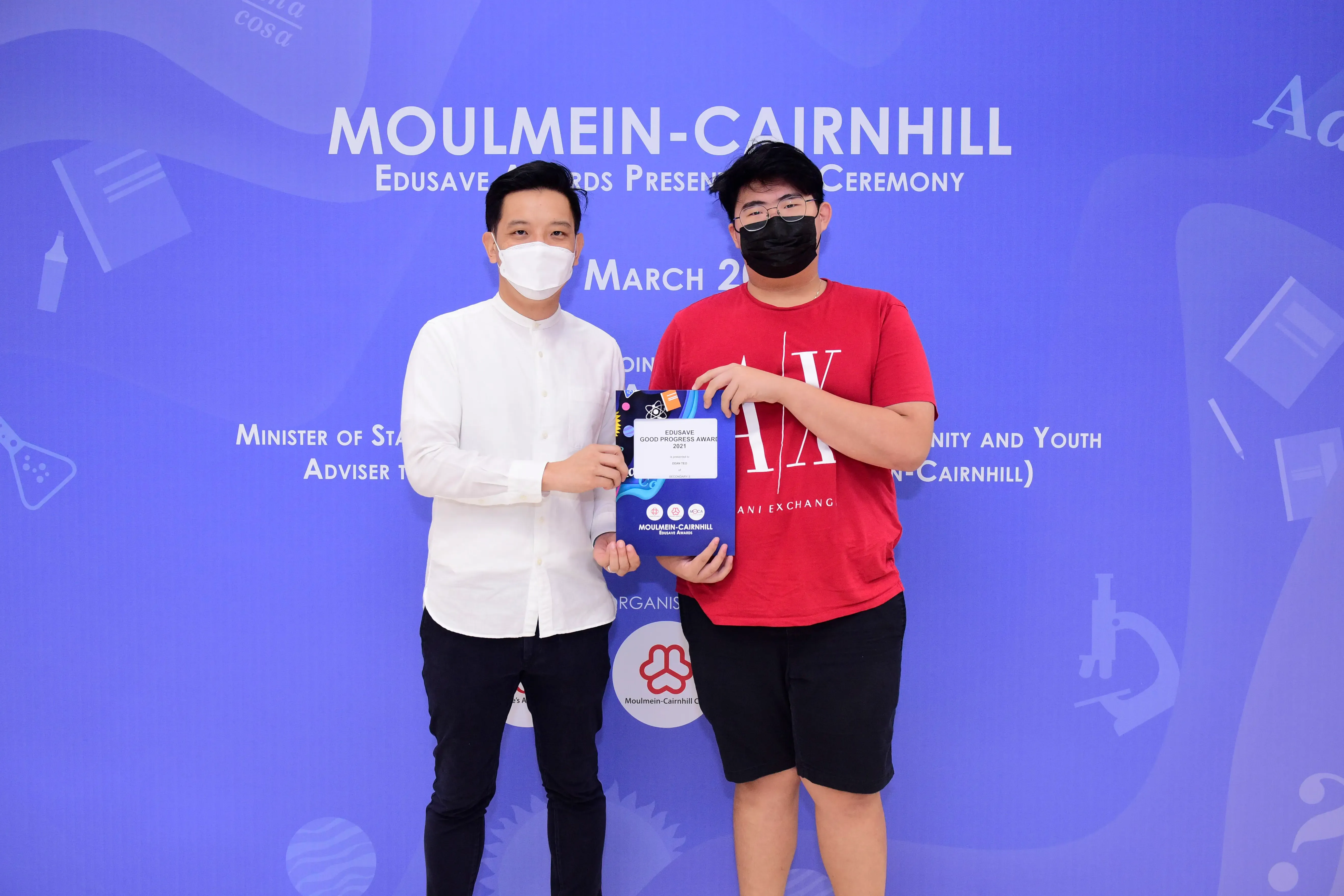 Two masked men hold an Edusave Good Progress Award at the Moulmein-Cairnhill Edusave Awards Ceremony.