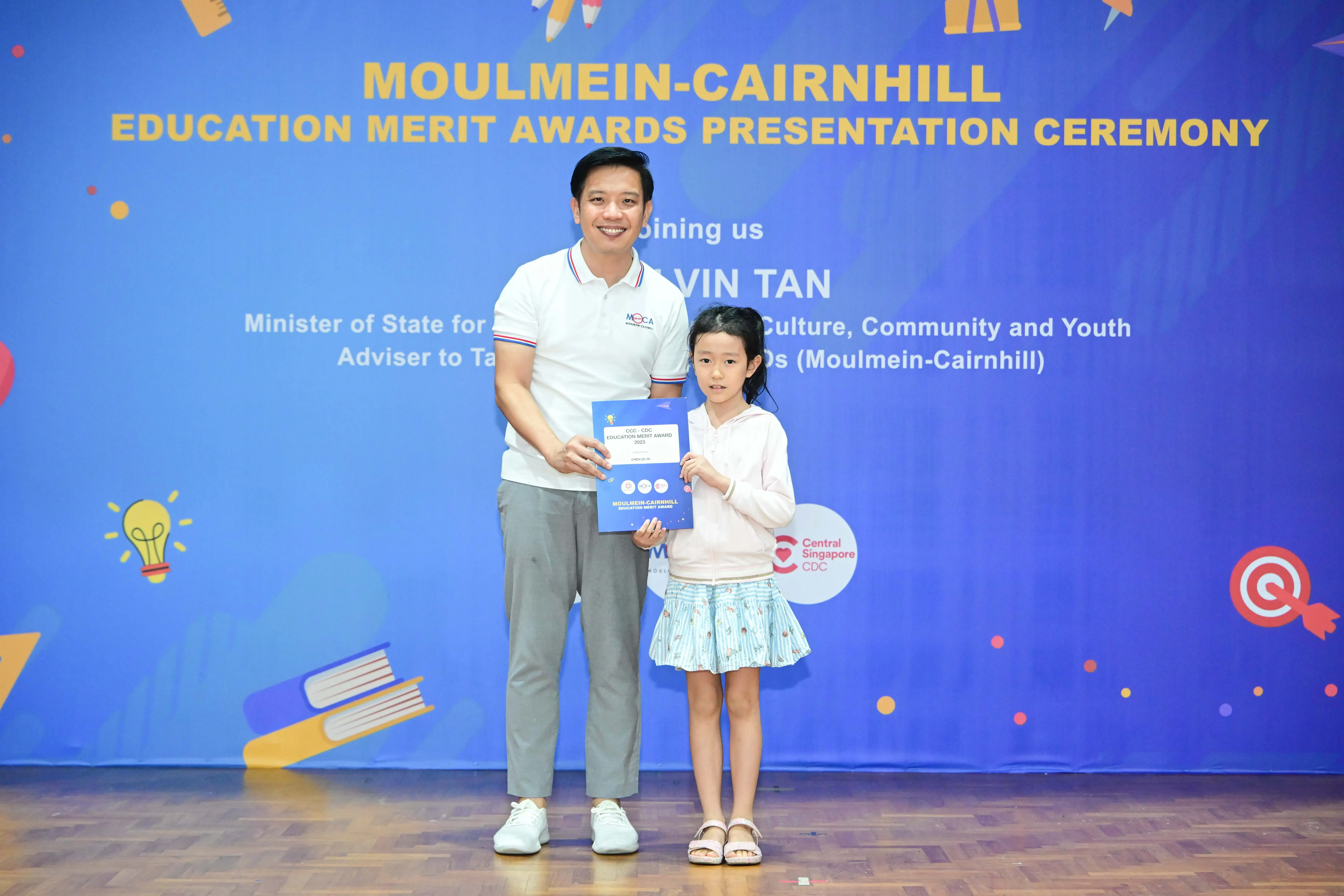 A man and a young girl hold an award certificate at the Moulmein-Cairnhill Education Merit Awards Presentation Ceremony.