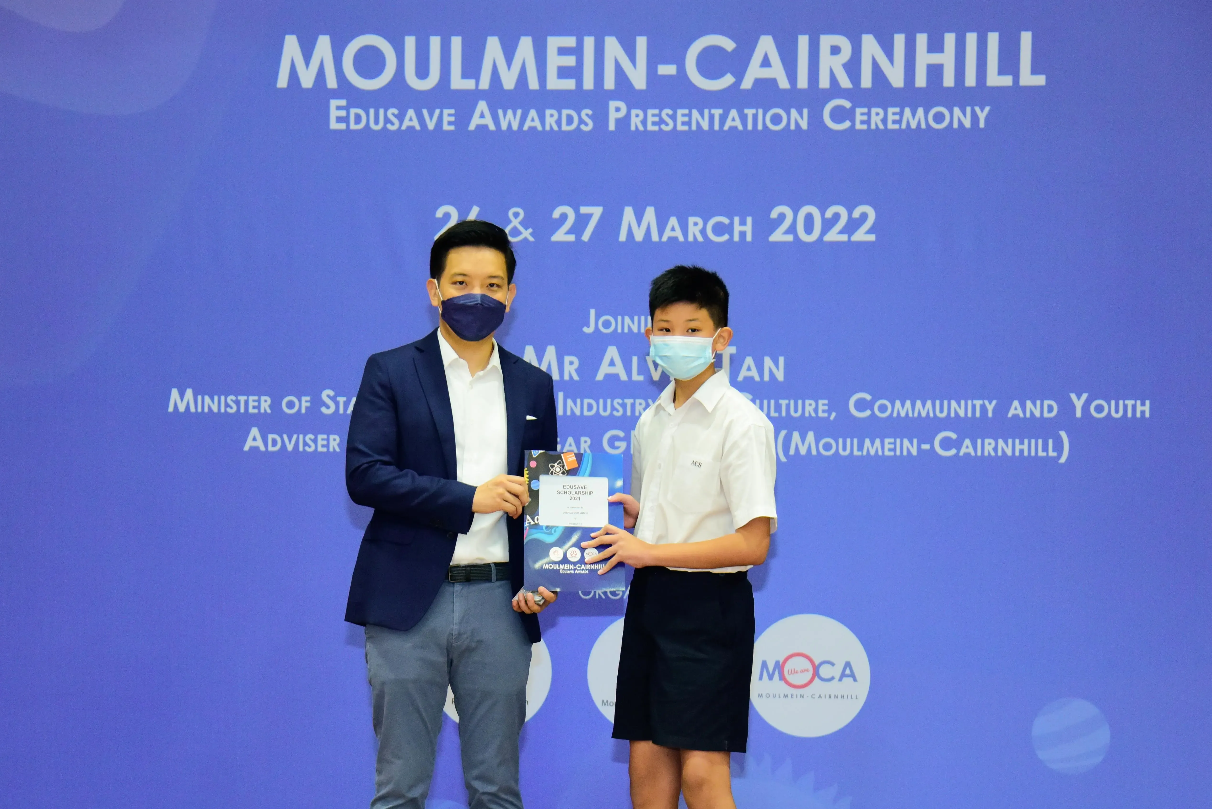 An adult and a young student in masks hold a certificate at the Moulmein-Cairnhill Edusave Awards Ceremony, March 2022.