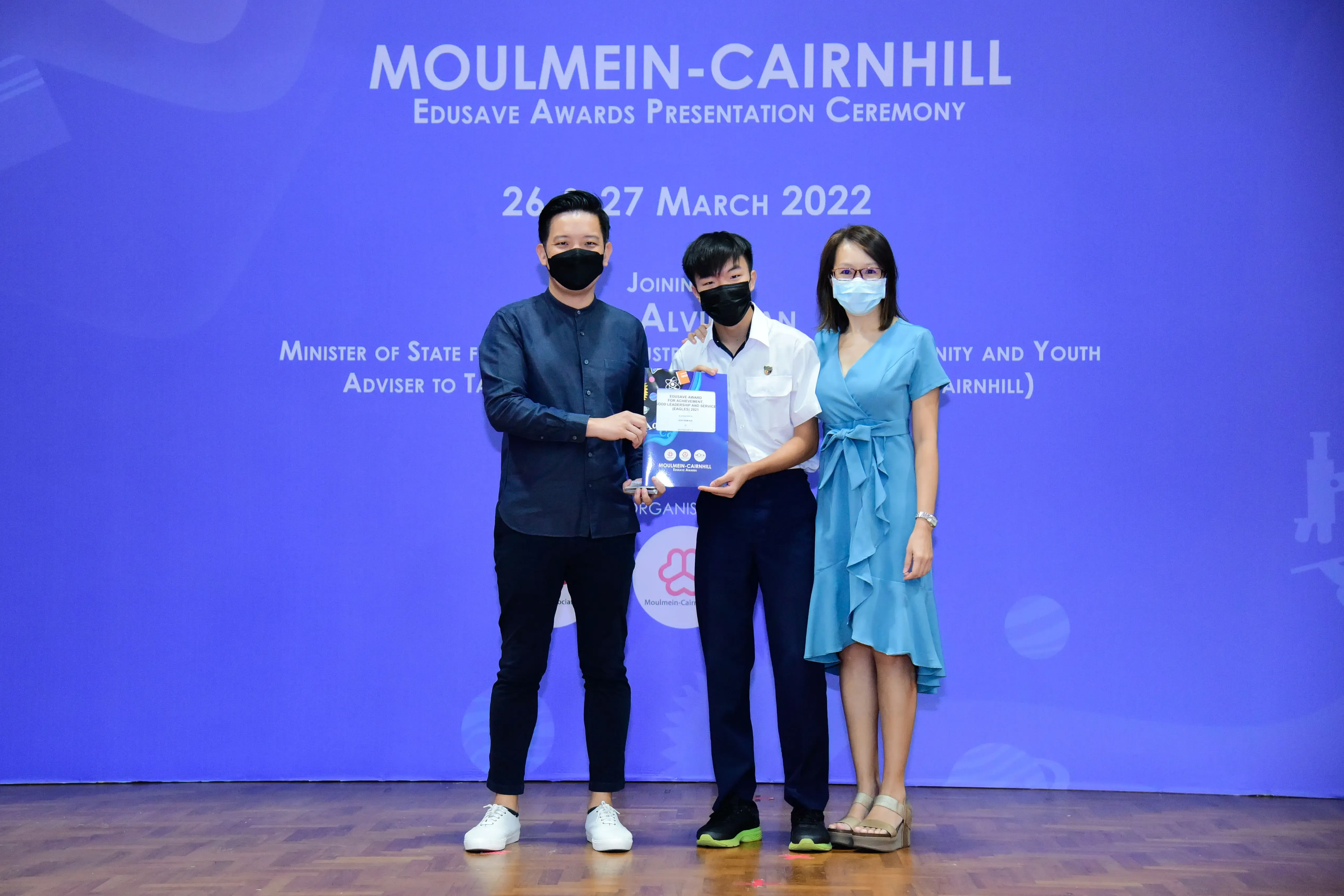 Three masked people pose holding an award at the Moulmein-Cairnhill Edusave Awards Ceremony, March 2022.