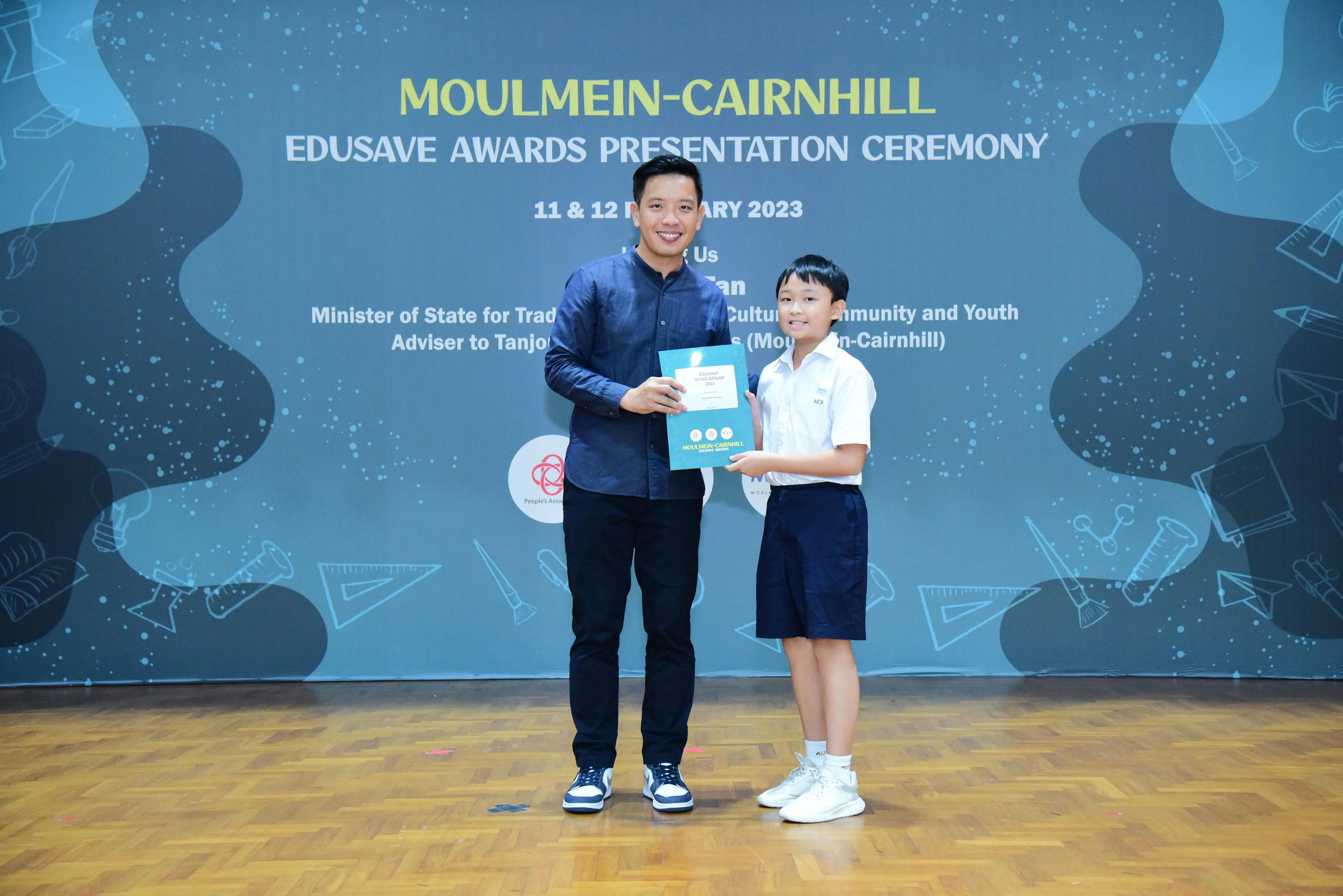 Adult man and young boy in school uniform hold a certificate at Moulmein-Cairnhill Edusave Awards Ceremony 2023.