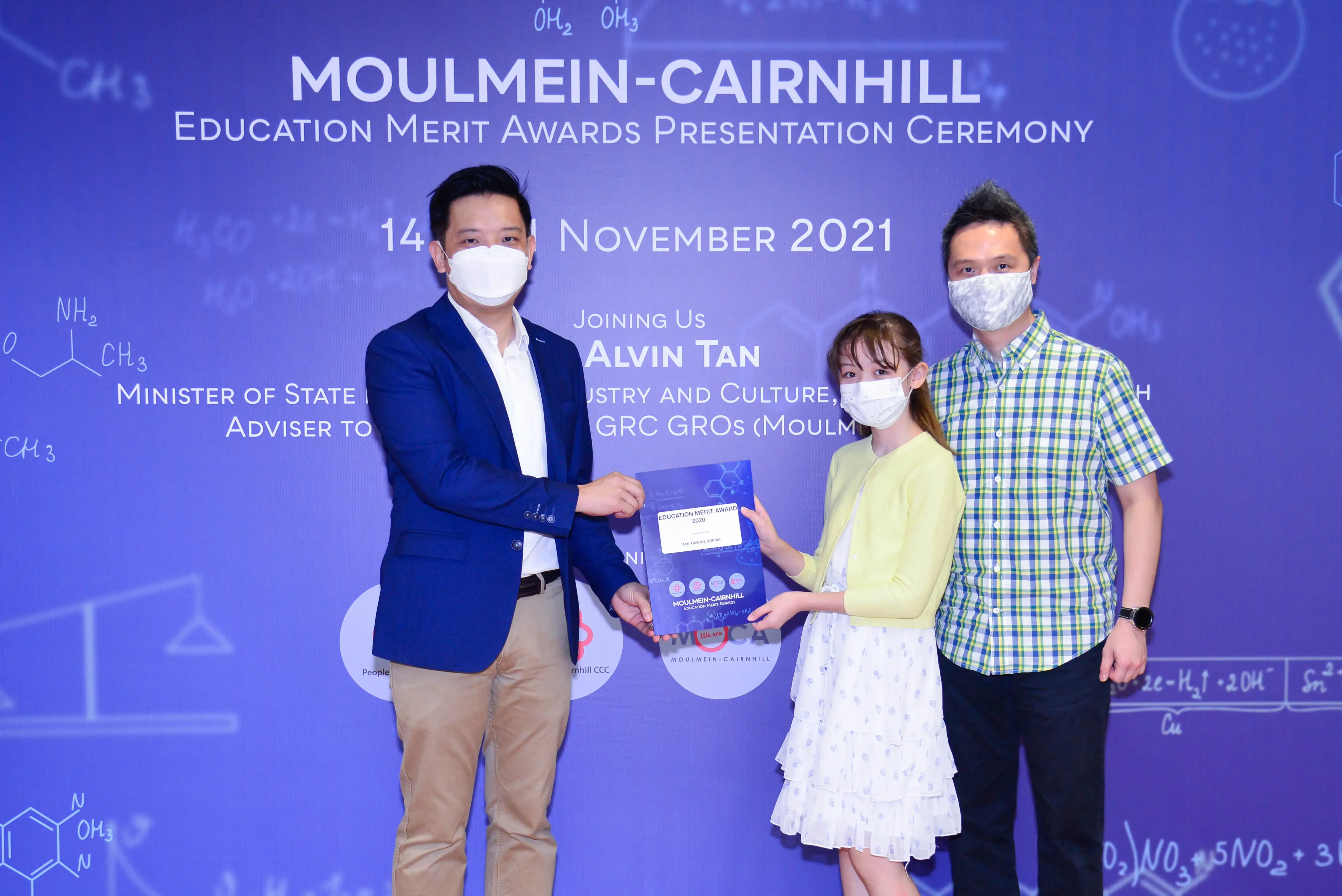 Three masked people at Moulmein-Cairnhill Education Merit Awards Ceremony on 14 November 2021, presenting a certificate.