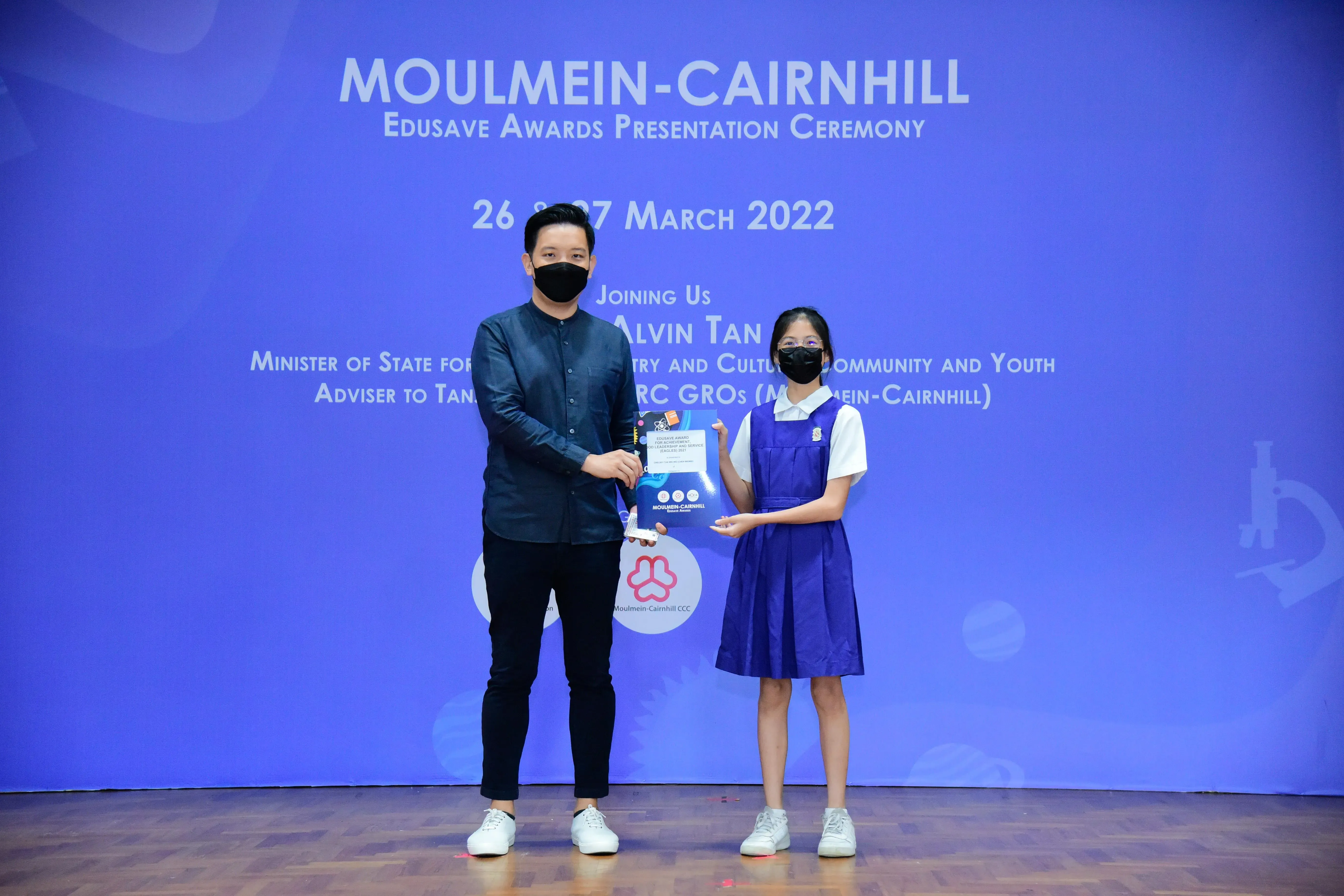 A man and a young girl in school uniform hold an award together at the Moulmein-Cairnhill Edusave Awards Ceremony 2022.