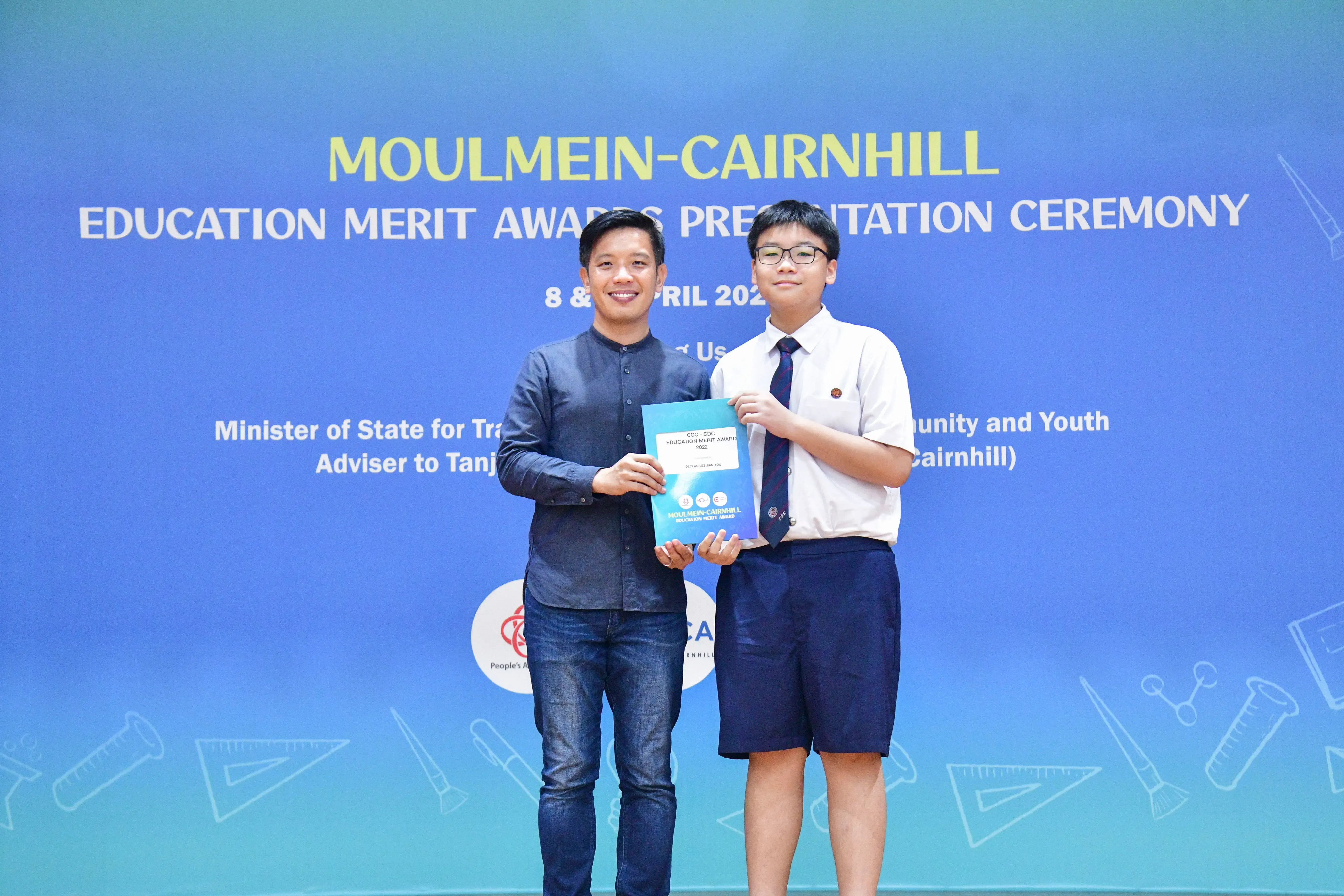 An adult and a school student hold an award booklet at the Moulmein-Cairnhill Education Merit Awards ceremony.