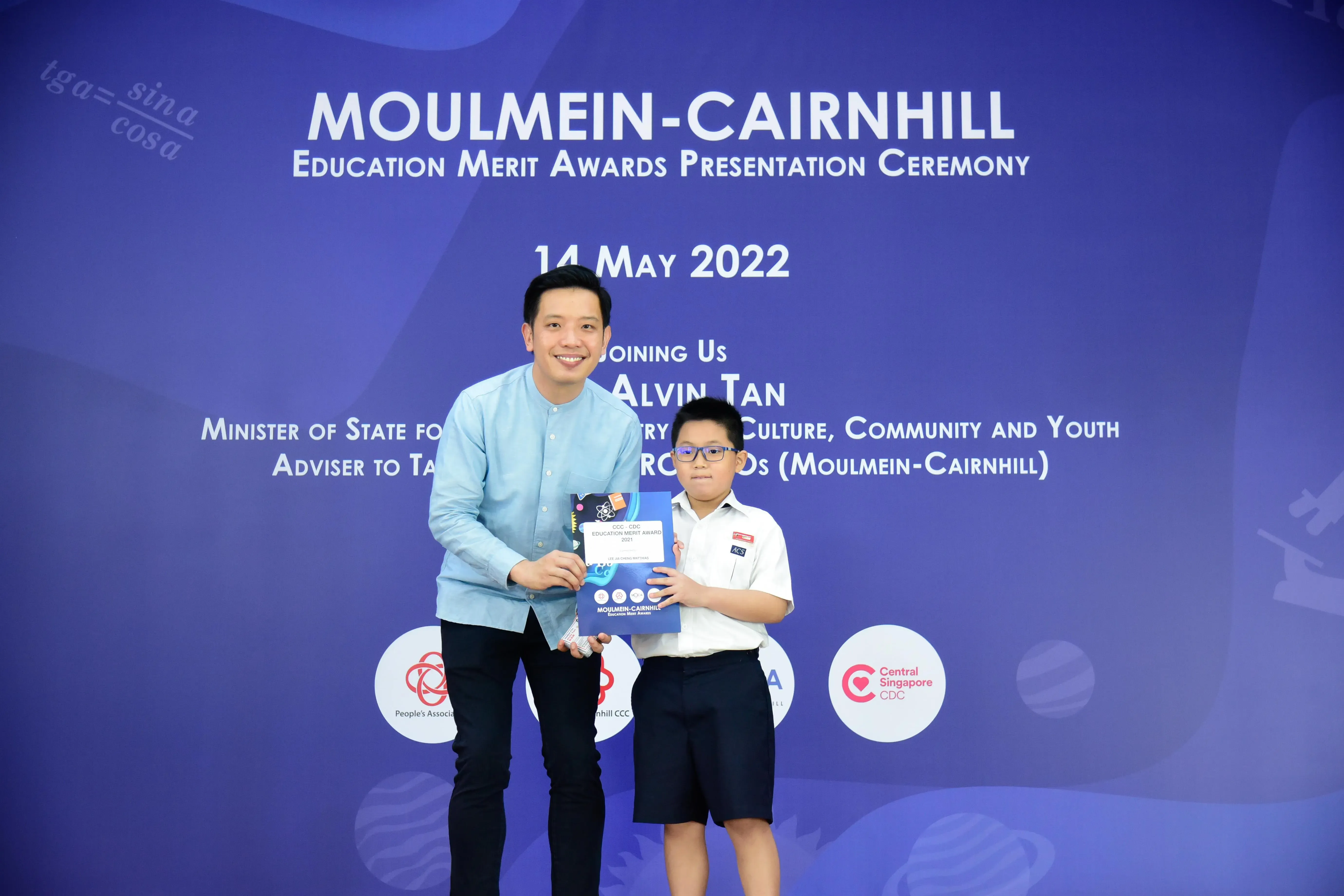A man and a young boy hold an award booklet at the Moulmein-Cairnhill Education Merit Awards ceremony on 14 May 2022.