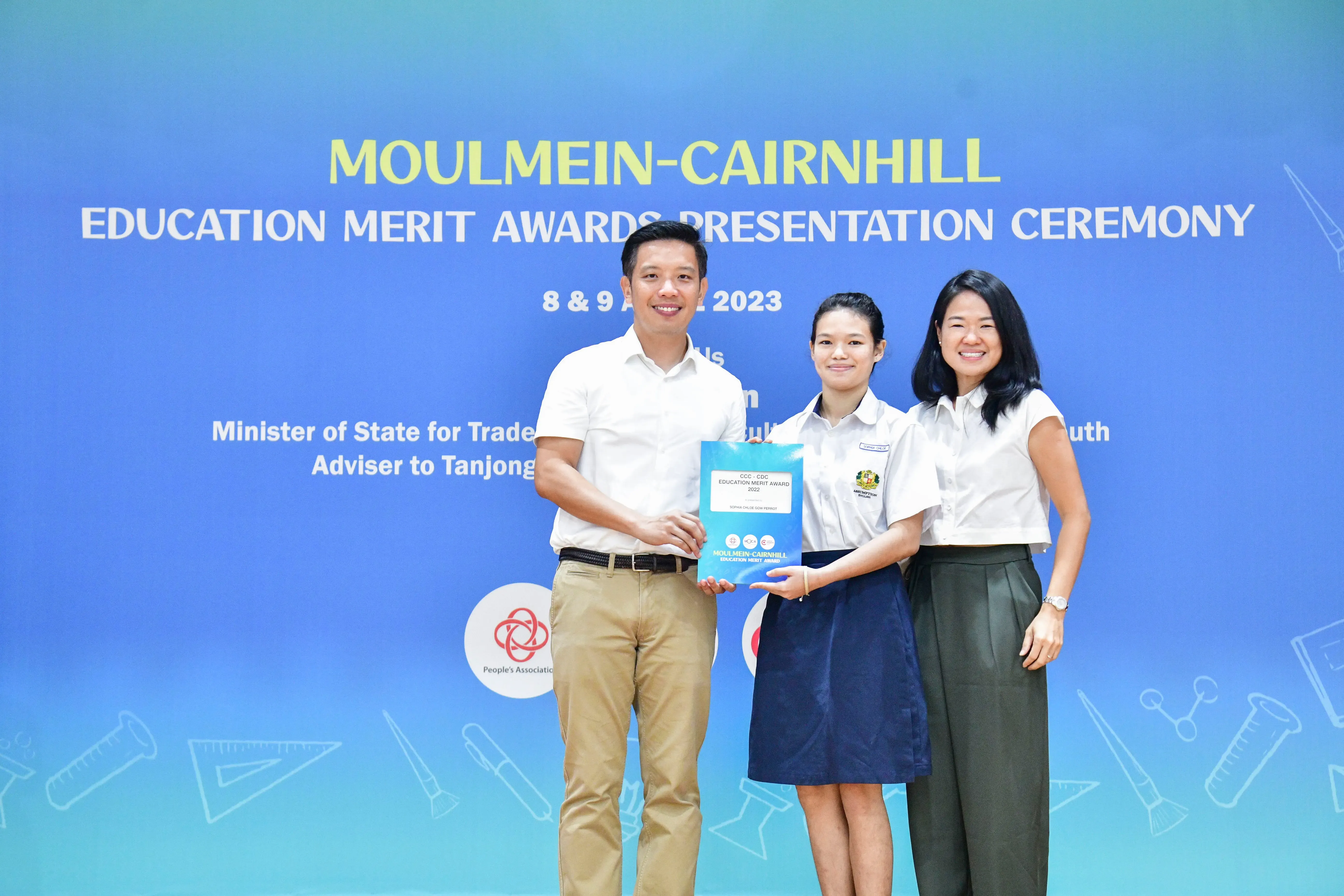Three people pose holding an award certificate at the Moulmein-Cairnhill Education Merit Awards Ceremony 2023.