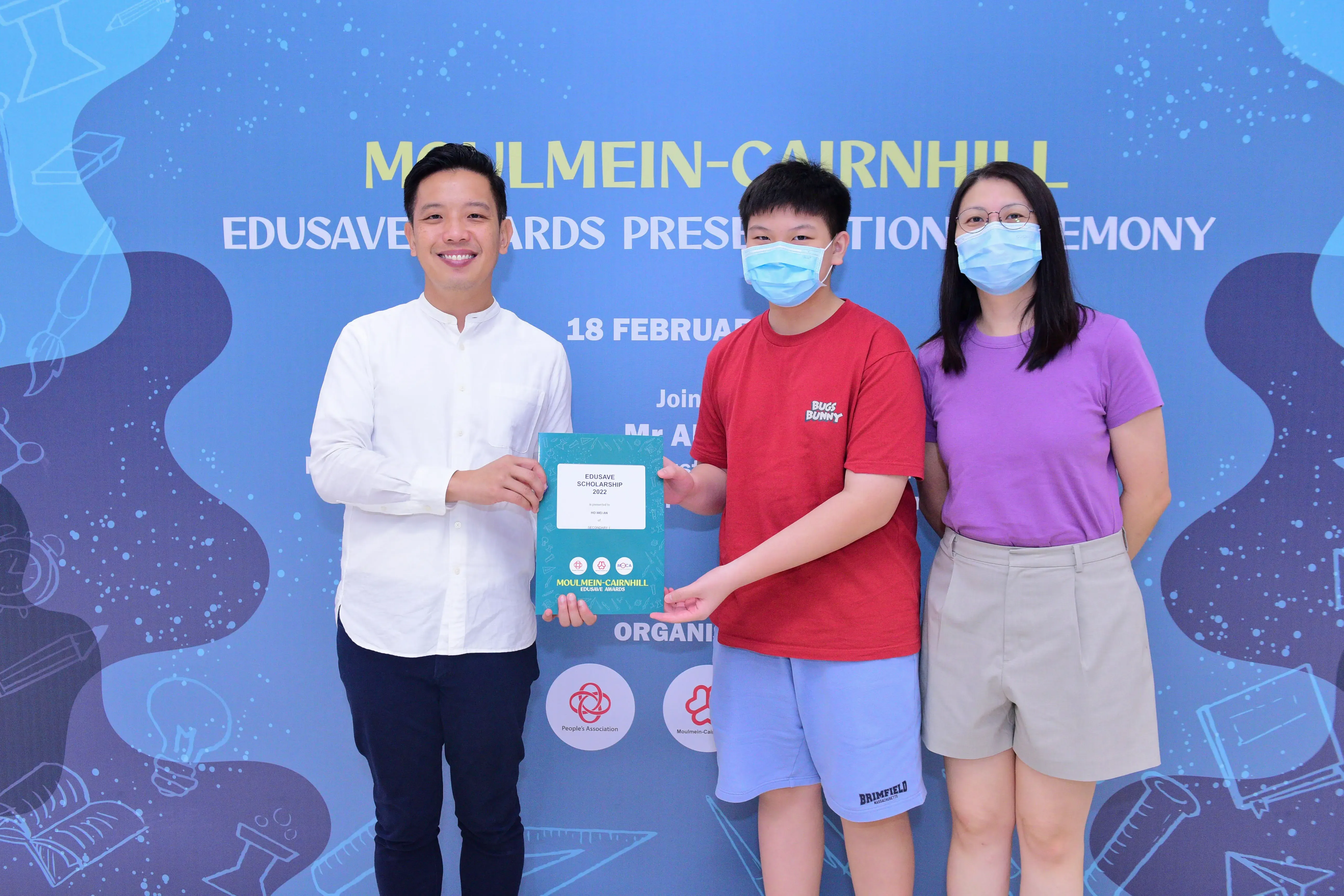 Three people pose at the Moulmein-Cairnhill Edusave Awards Presentation Ceremony, holding a 2022 scholarship certificate.