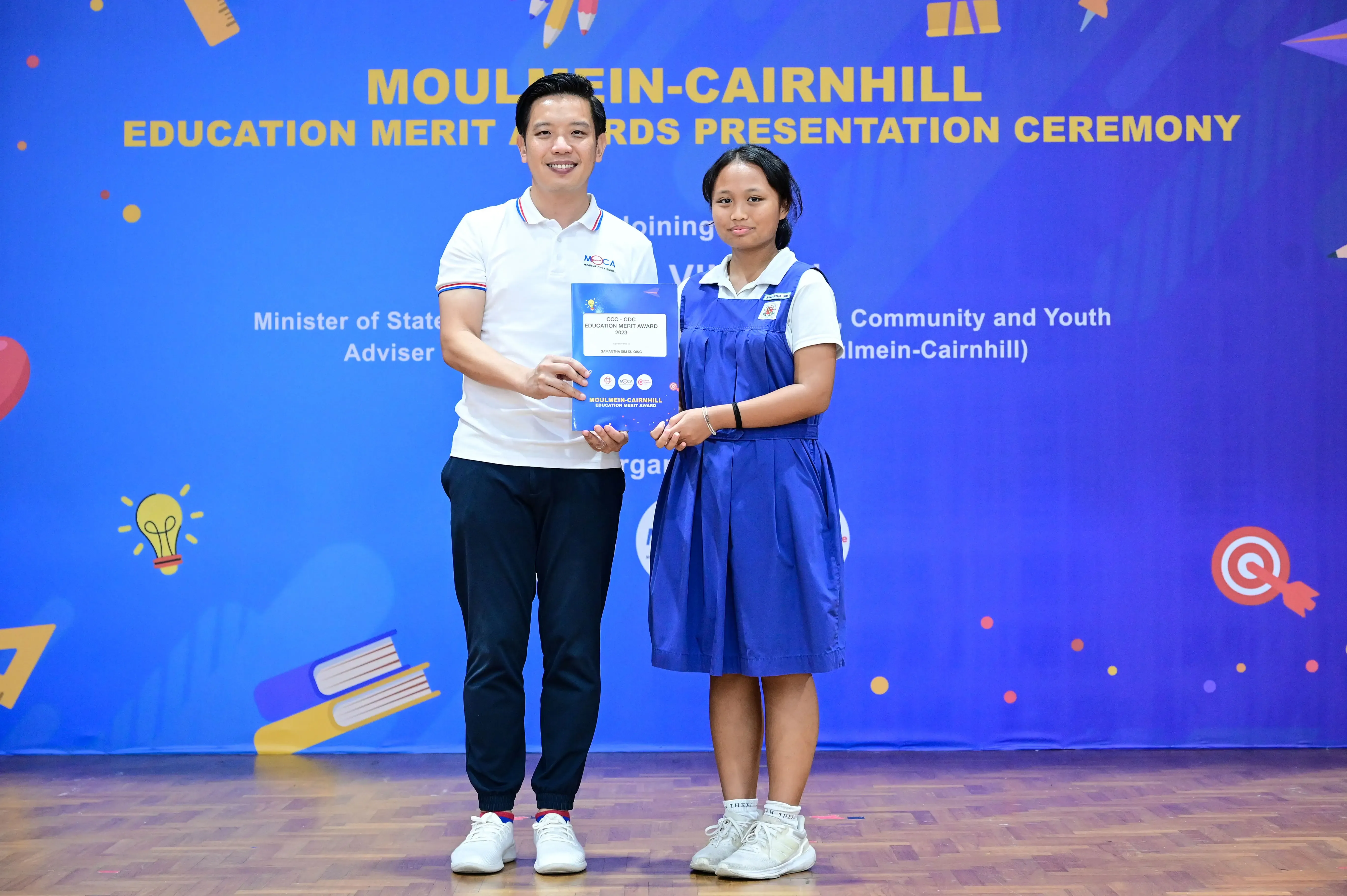 A man and a girl in school uniform hold a certificate at the Moulmein-Cairnhill Education Merit Awards ceremony.