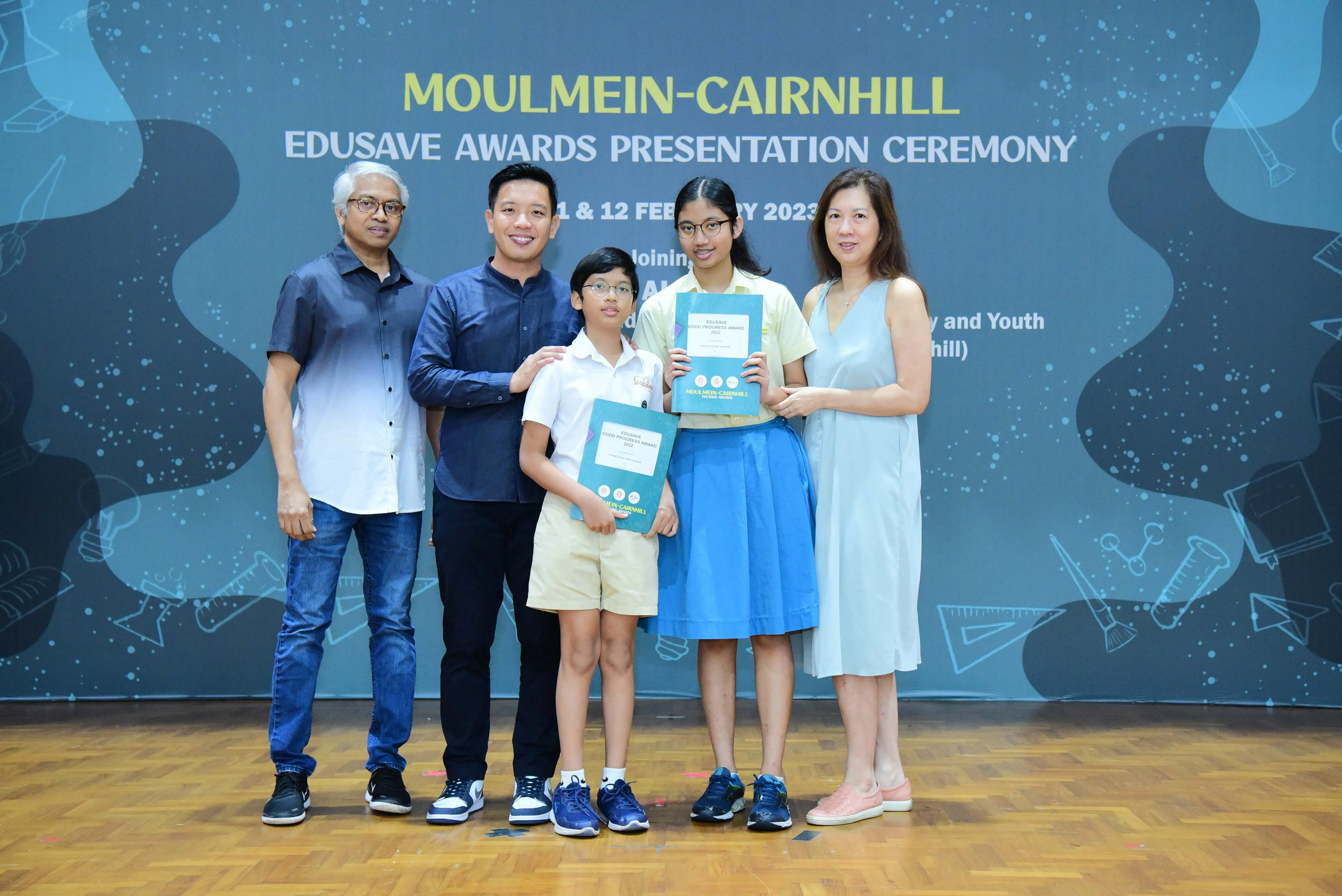 Five people pose at the Moulmein-Cairnhill Edusave Awards Presentation Ceremony 2023, two children holding award folders.