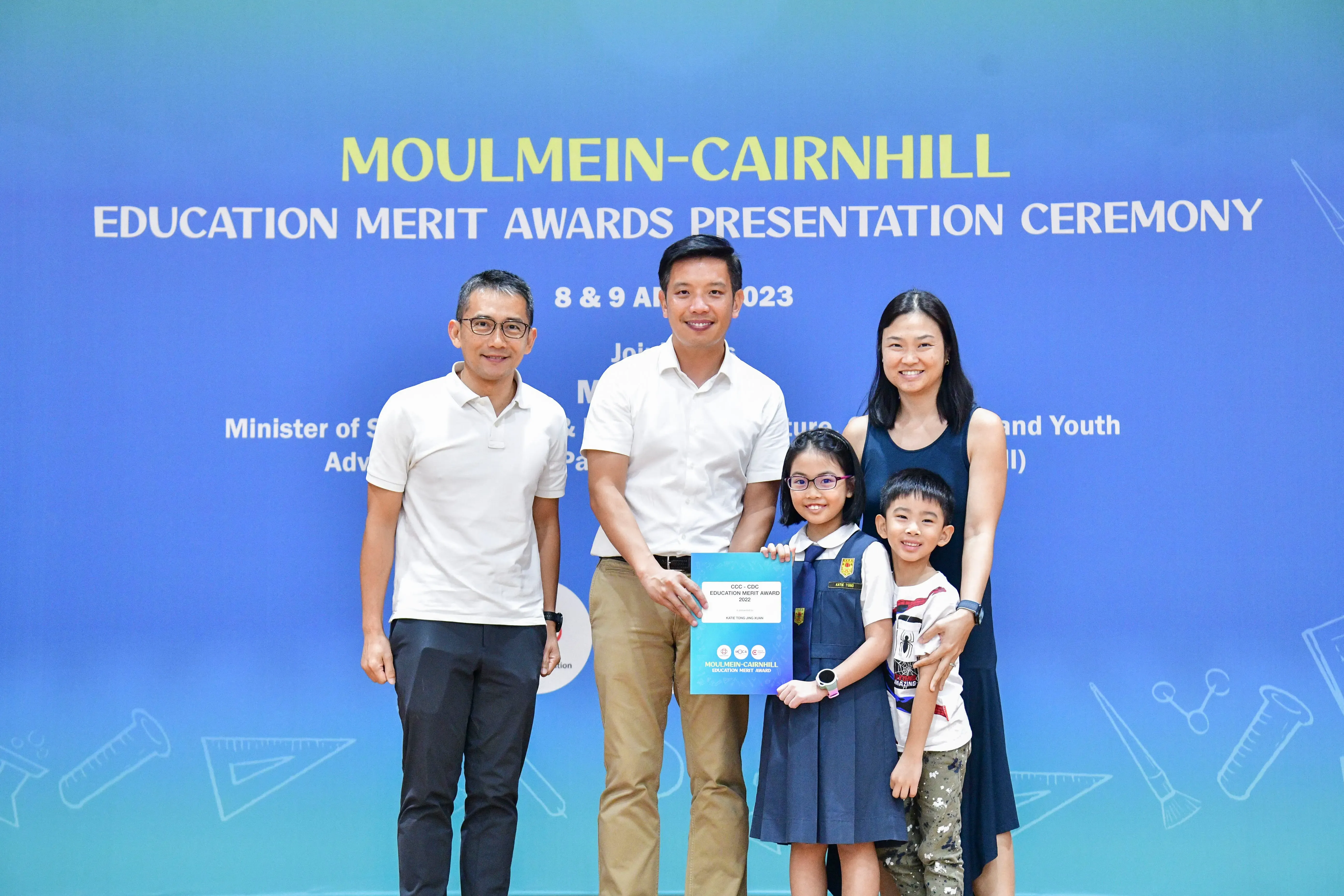 Two adults and two children pose with an award certificate at the Moulmein-Cairnhill Education Merit Awards Ceremony 2023.
