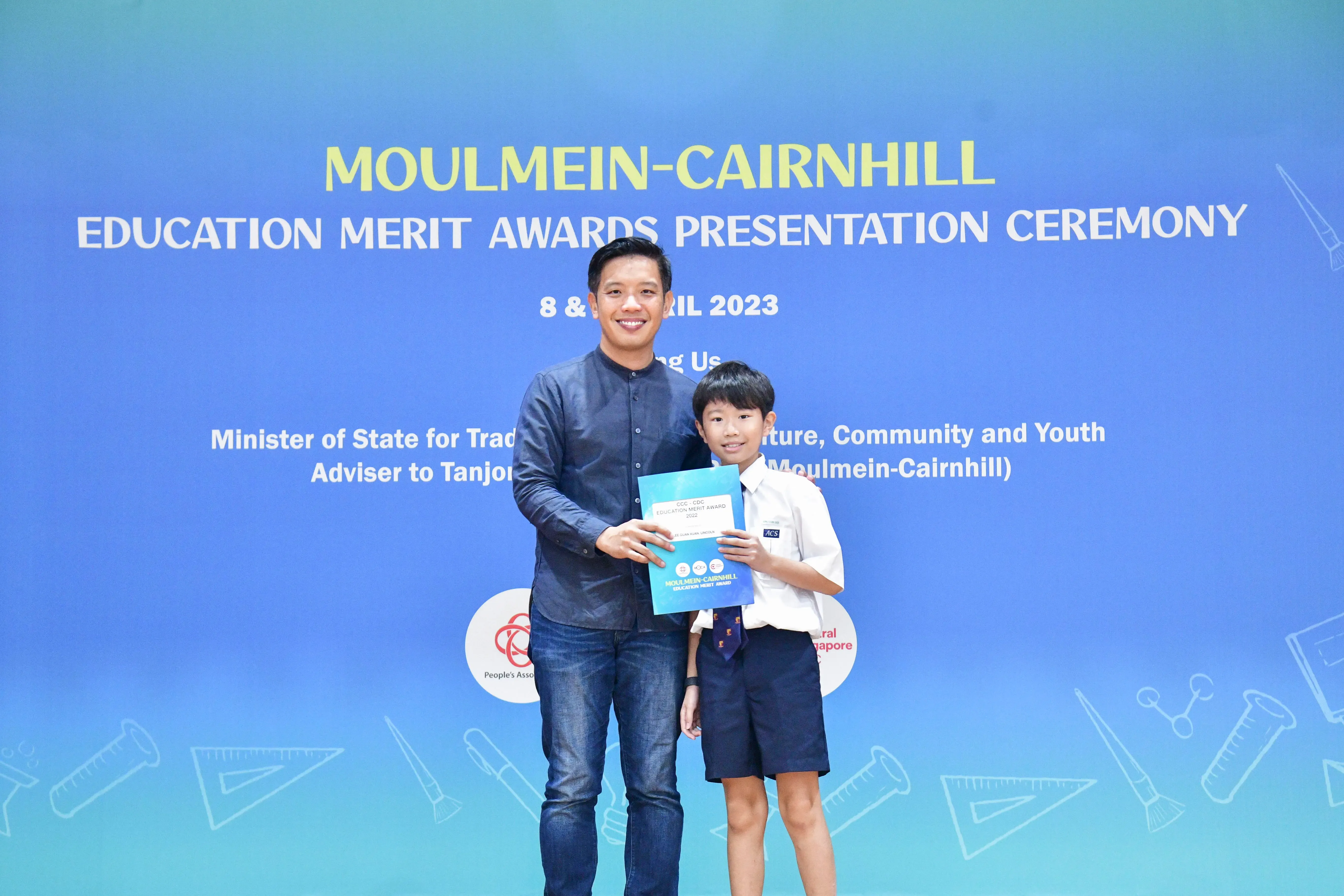 A man and a young boy hold a certificate together at the Moulmein-Cairnhill Education Merit Awards Ceremony 2023.