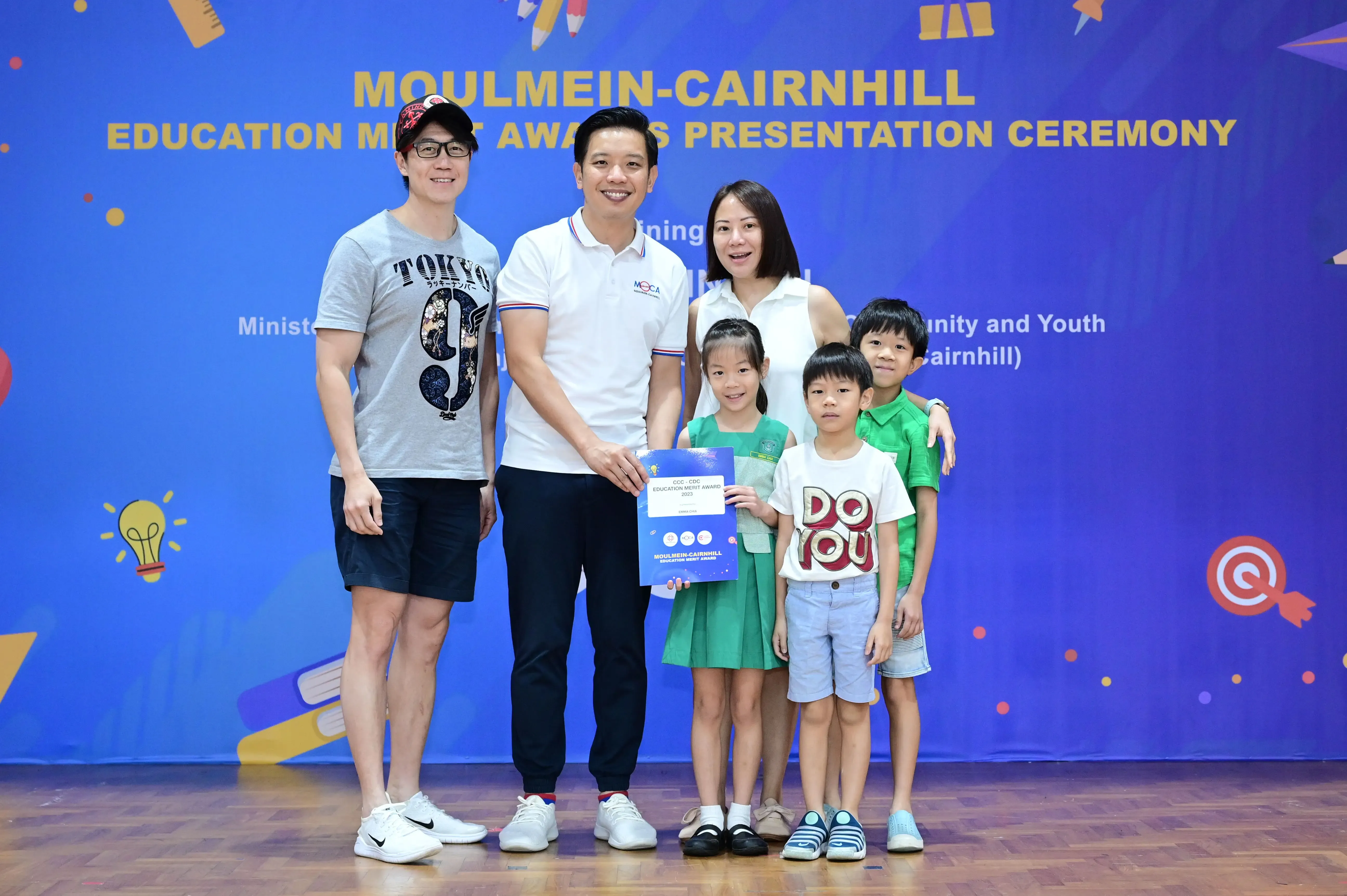 Two adults and three children pose with an award certificate at the Moulmein-Cairnhill Education Merit Awards Ceremony.