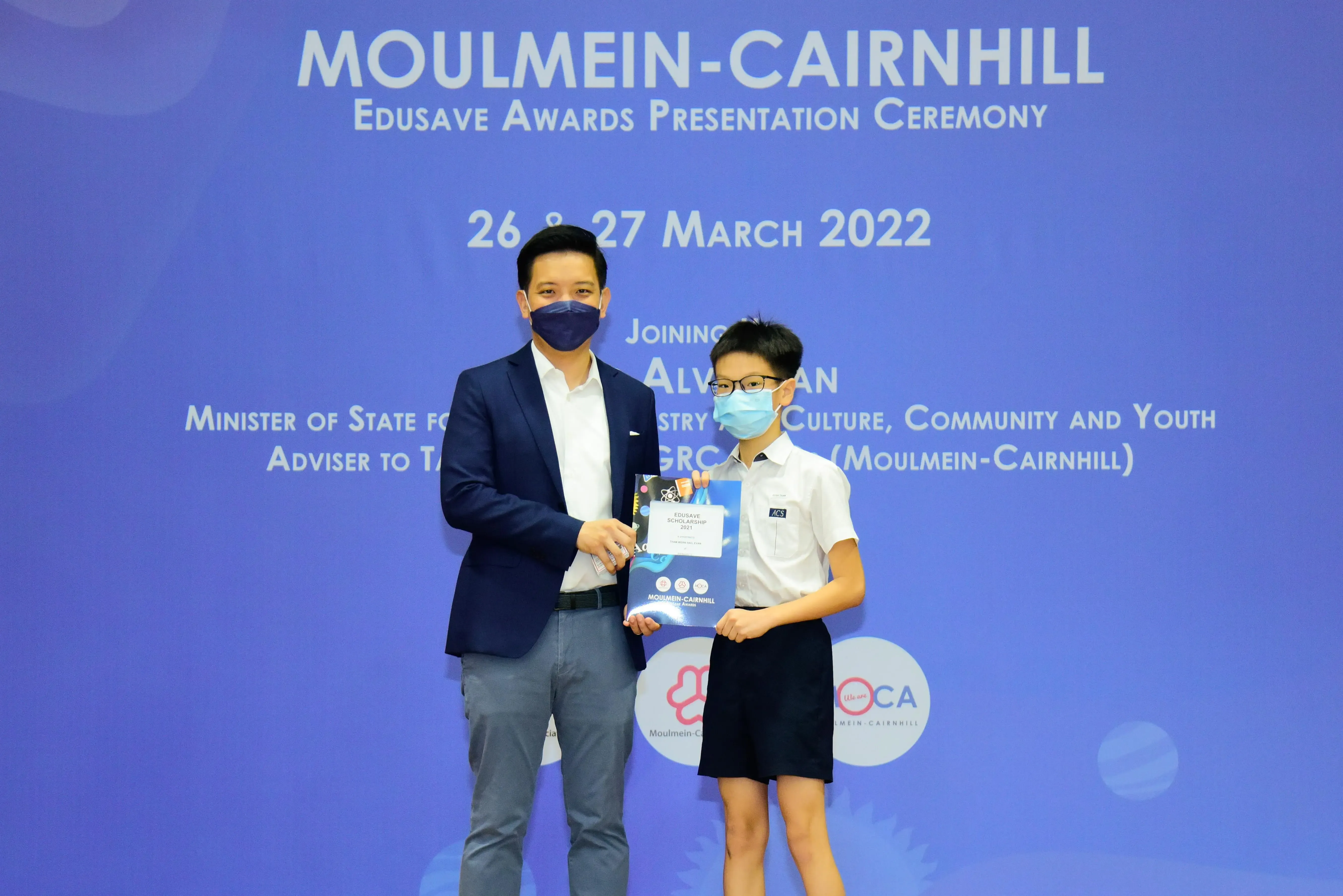 Two masked individuals hold an award folder at the Moulmein-Cairnhill Edusave Awards Ceremony, March 2022.