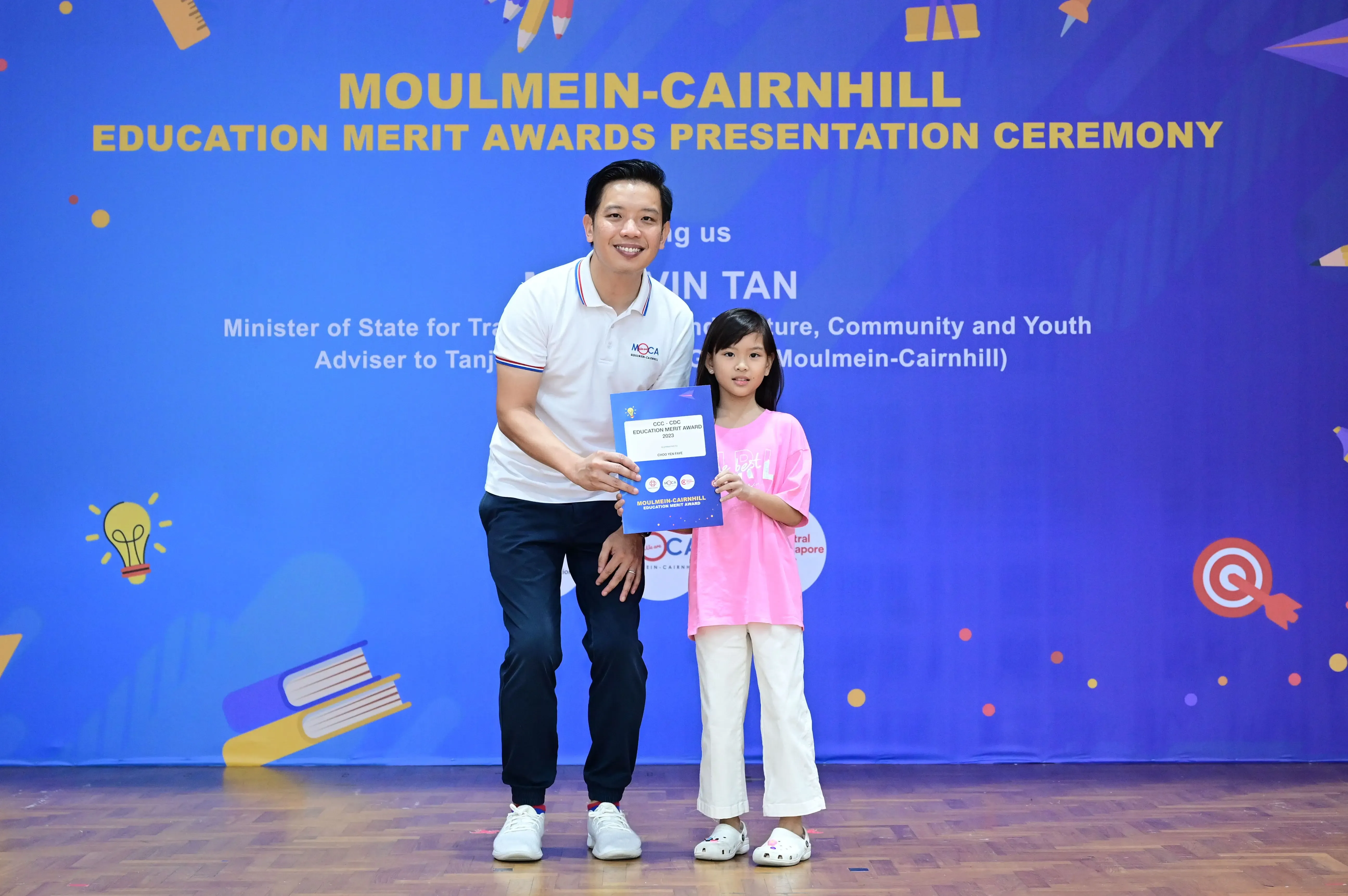 A man and a young girl hold a certificate at the Moulmein-Cairnhill Education Merit Awards Presentation Ceremony.