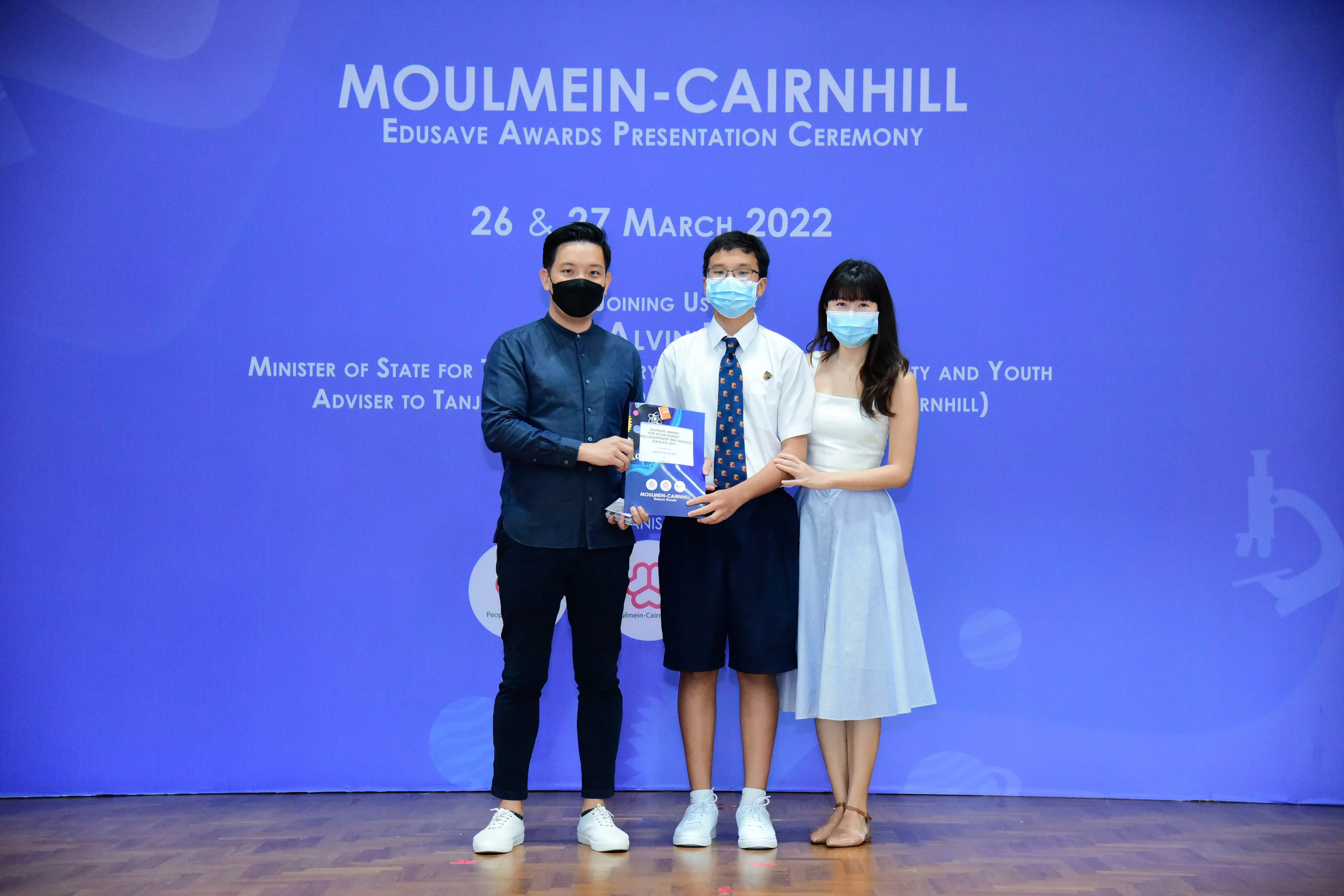 Three masked people pose holding an award at the Moulmein-Cairnhill Edusave Awards Ceremony, March 2022.