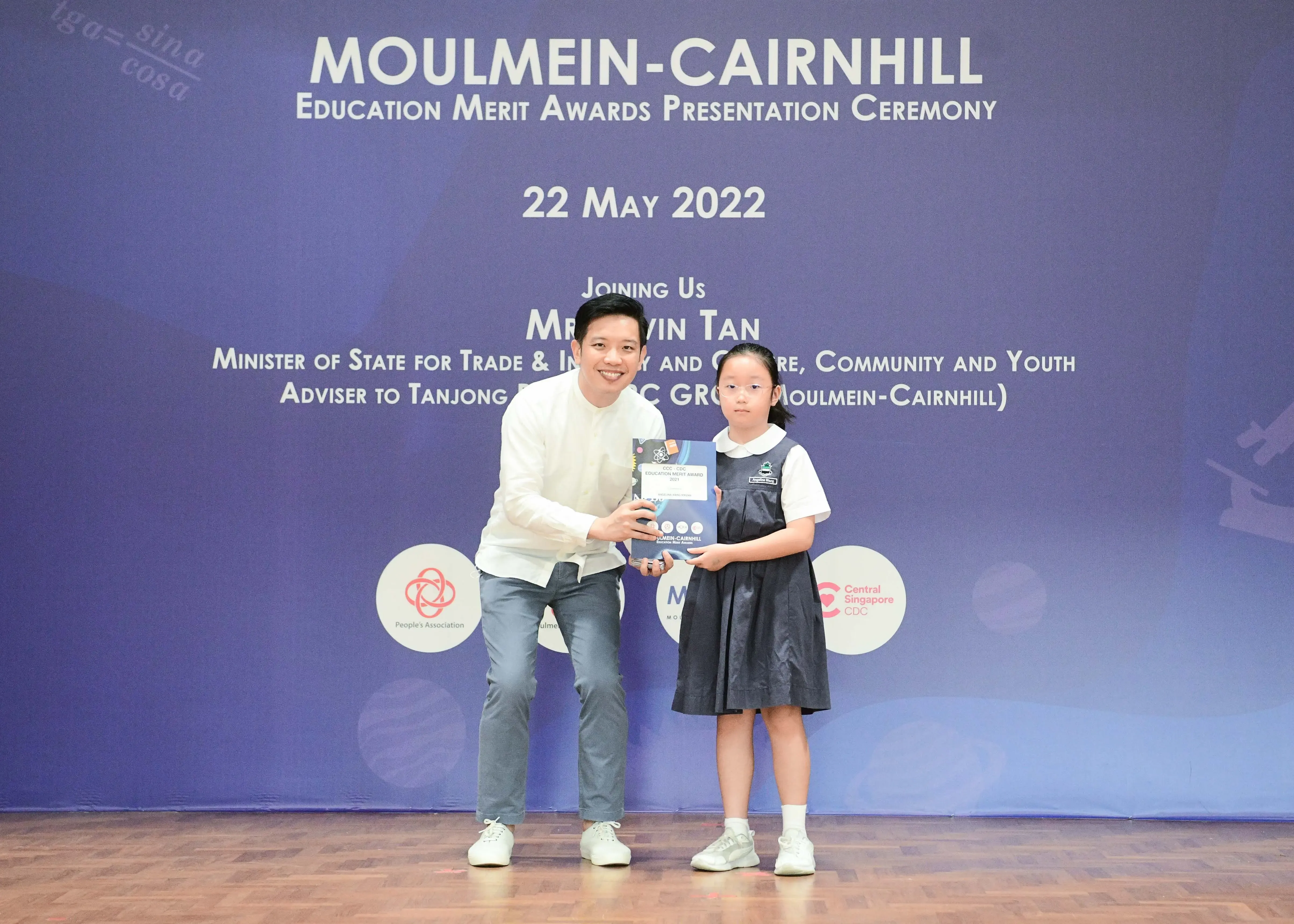 A man and a young girl in school uniform hold an award at the Moulmein-Cairnhill Education Merit Awards ceremony.