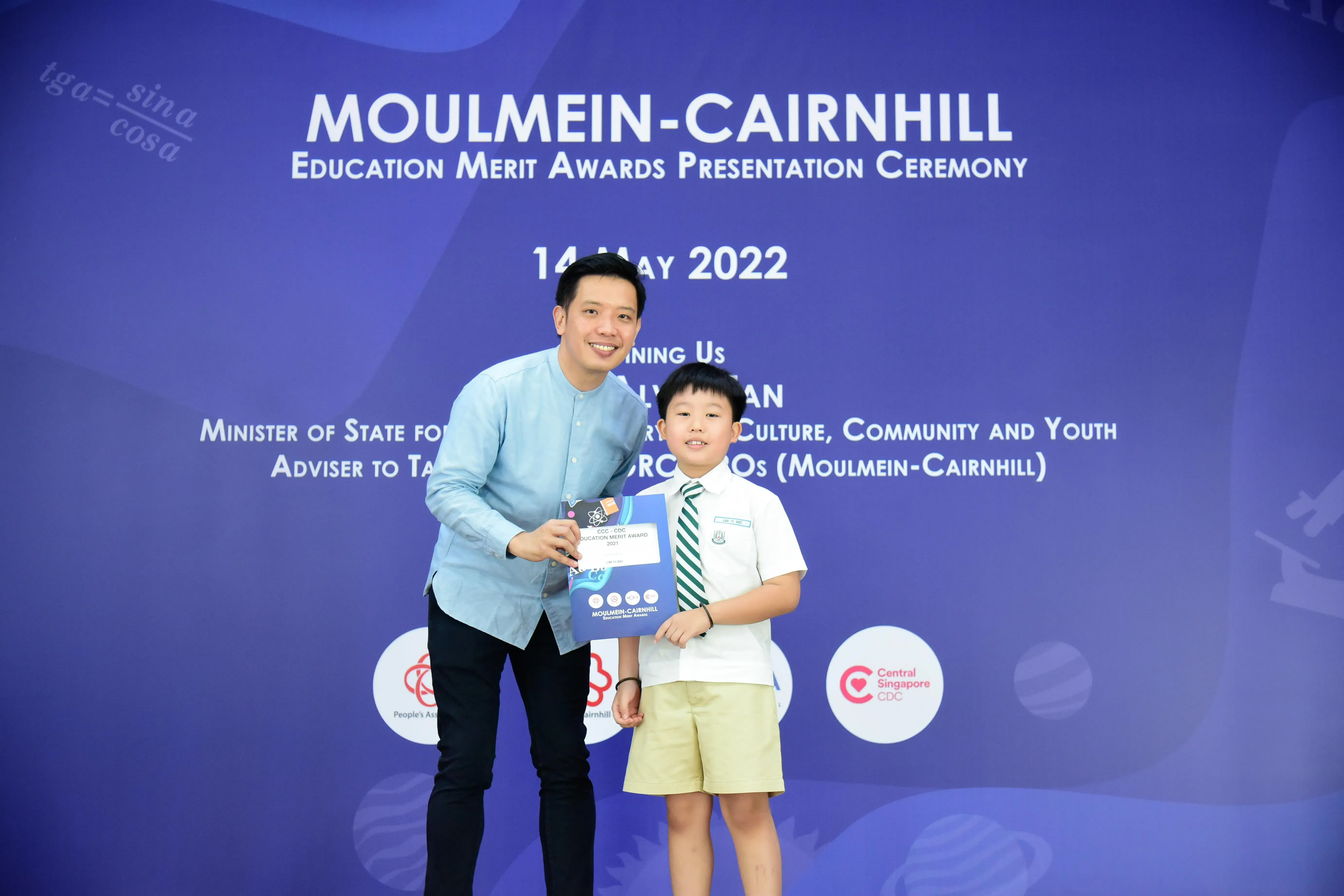 An adult and a young boy hold an award at the Moulmein-Cairnhill Education Merit Awards Ceremony, 14 May 2022.