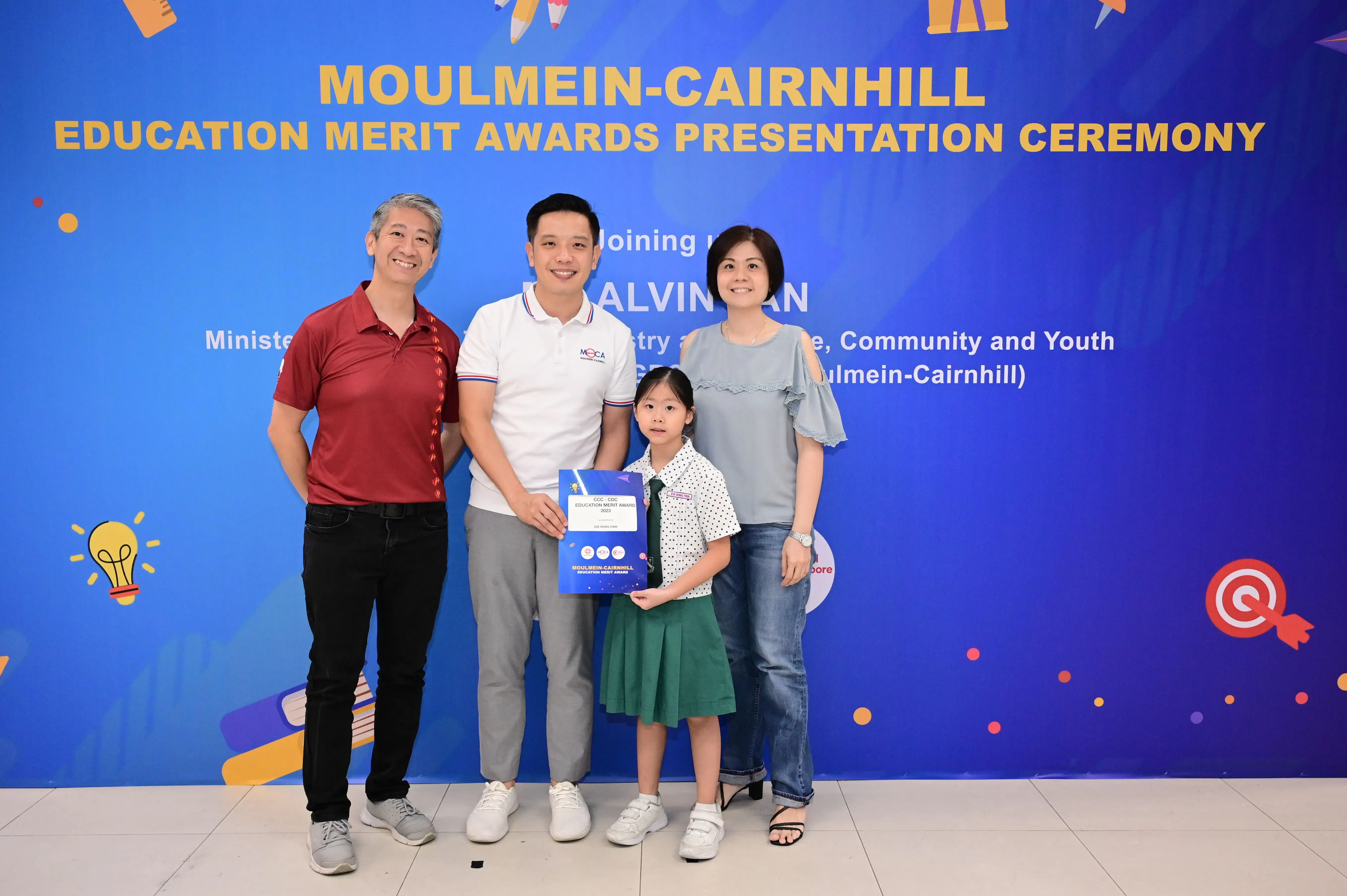 Three adults and a young girl pose with an award certificate at the Moulmein-Cairnhill Education Merit Awards ceremony.