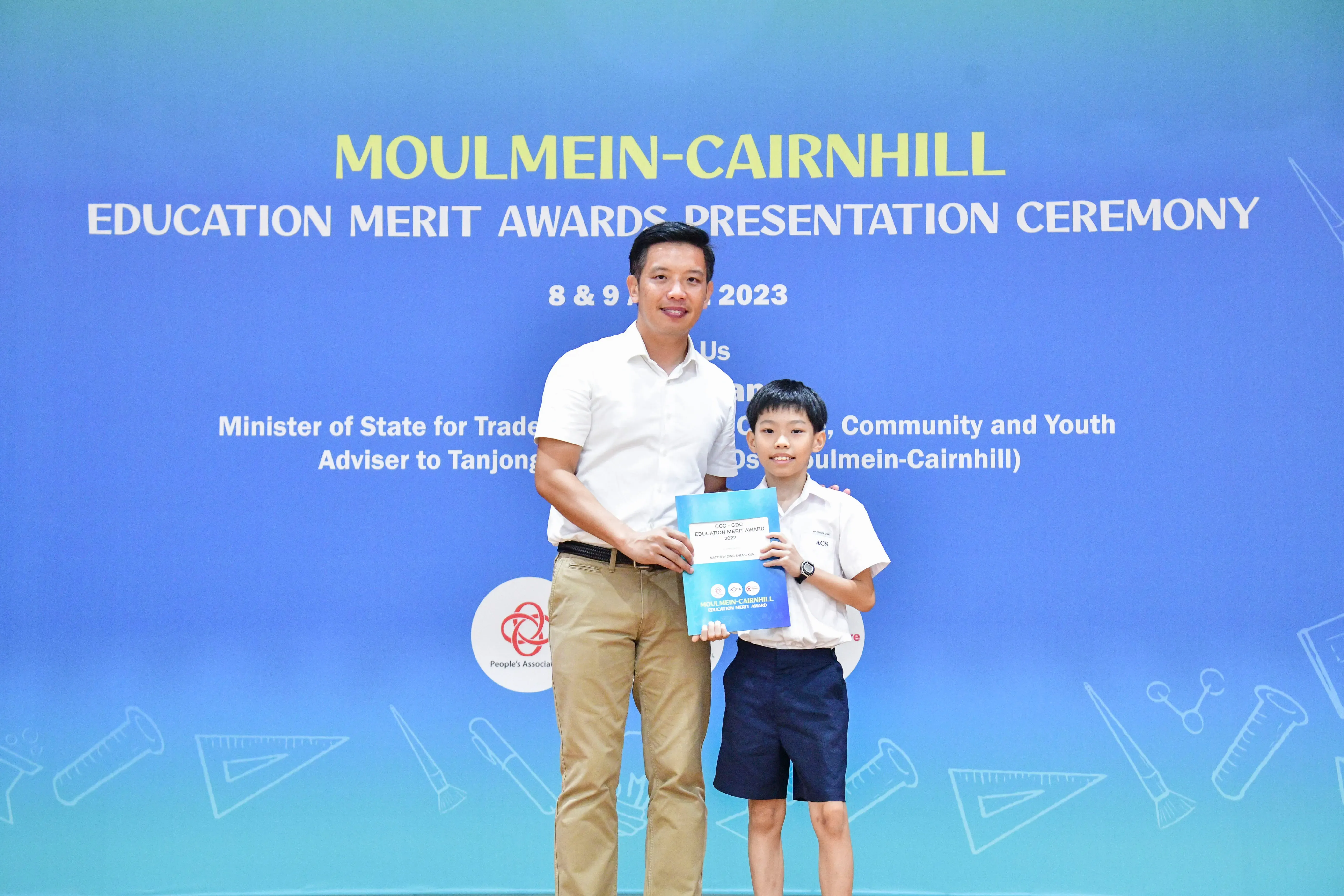 An adult and a young boy hold an award certificate at the Moulmein-Cairnhill Education Merit Awards Ceremony 2023.