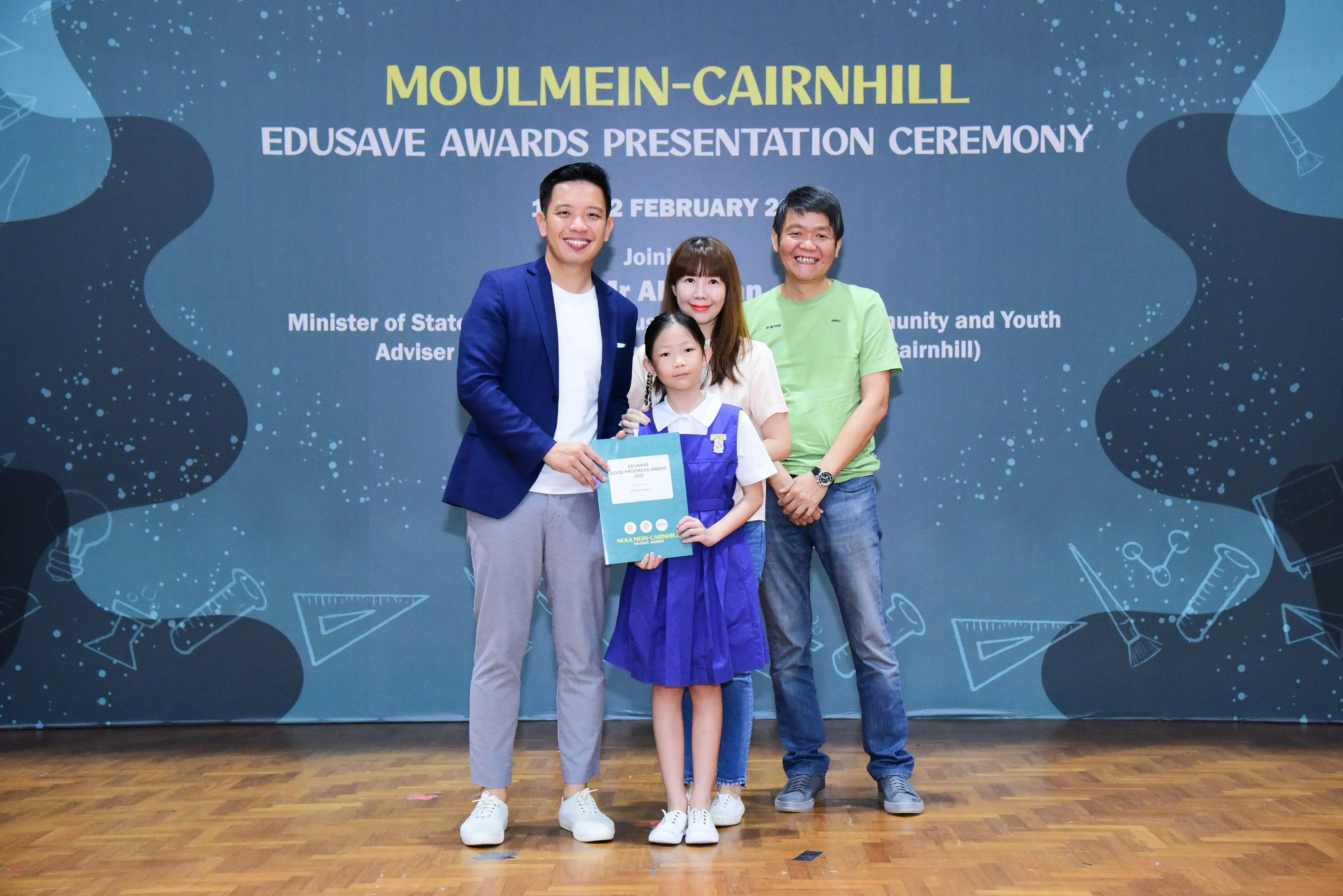 Four people pose at the Moulmein-Cairnhill Edusave Awards Presentation Ceremony, with a young girl holding a certificate.