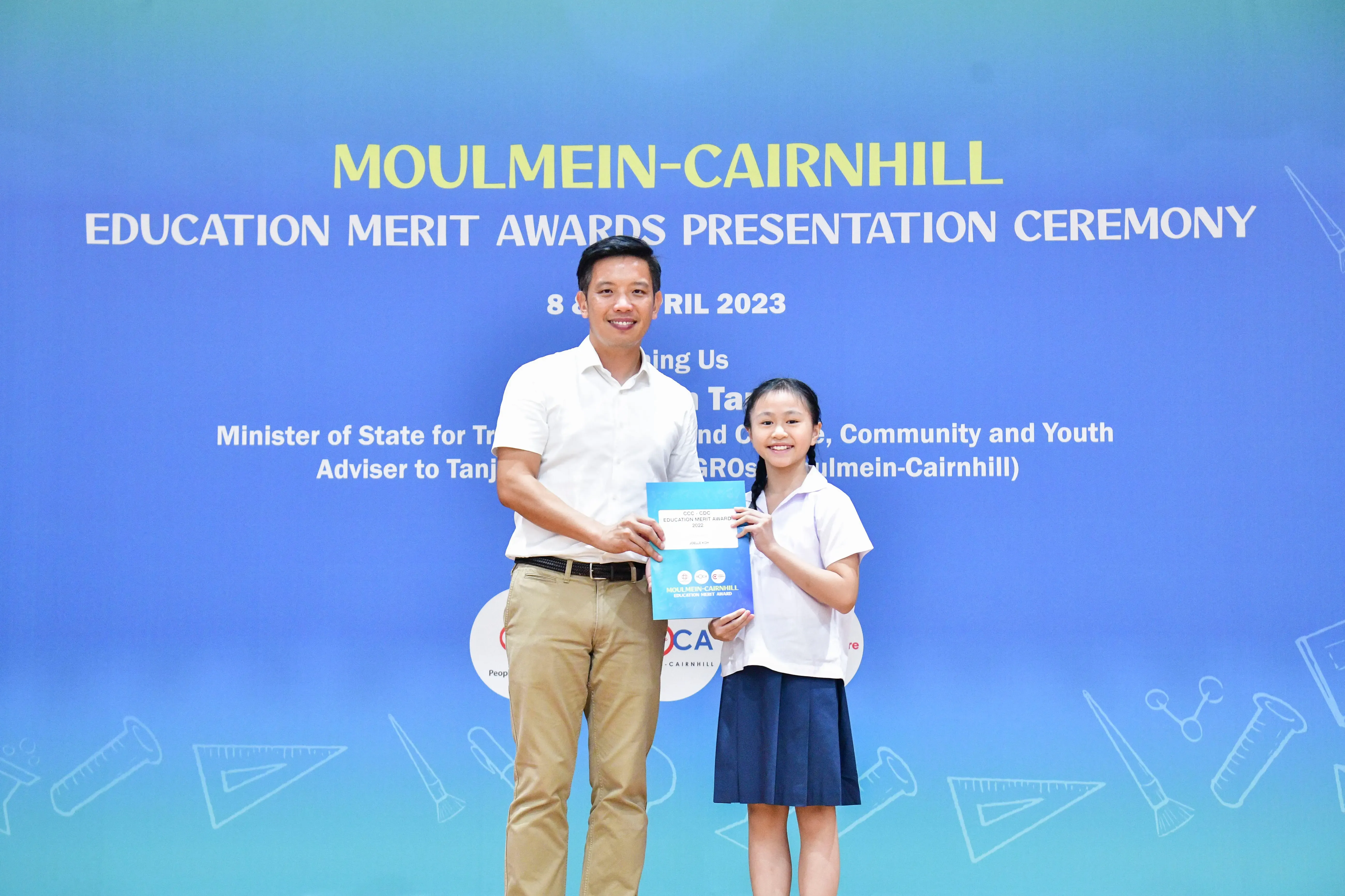 A man and a young girl in school uniform hold a certificate at the Moulmein-Cairnhill Education Merit Awards 2023.