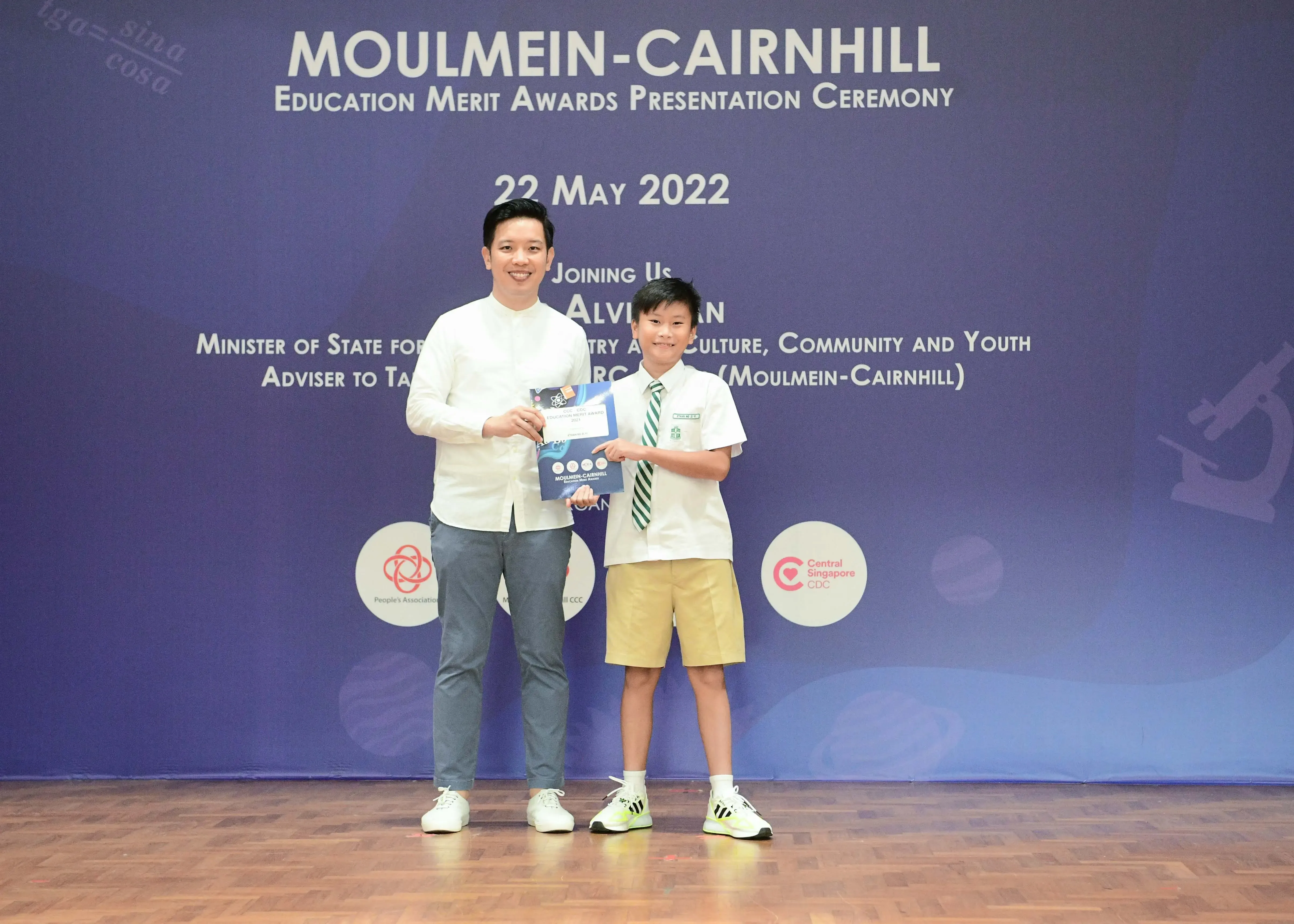 Man and young boy in school uniform hold an award at Moulmein-Cairnhill Education Merit Awards Ceremony, May 2022.