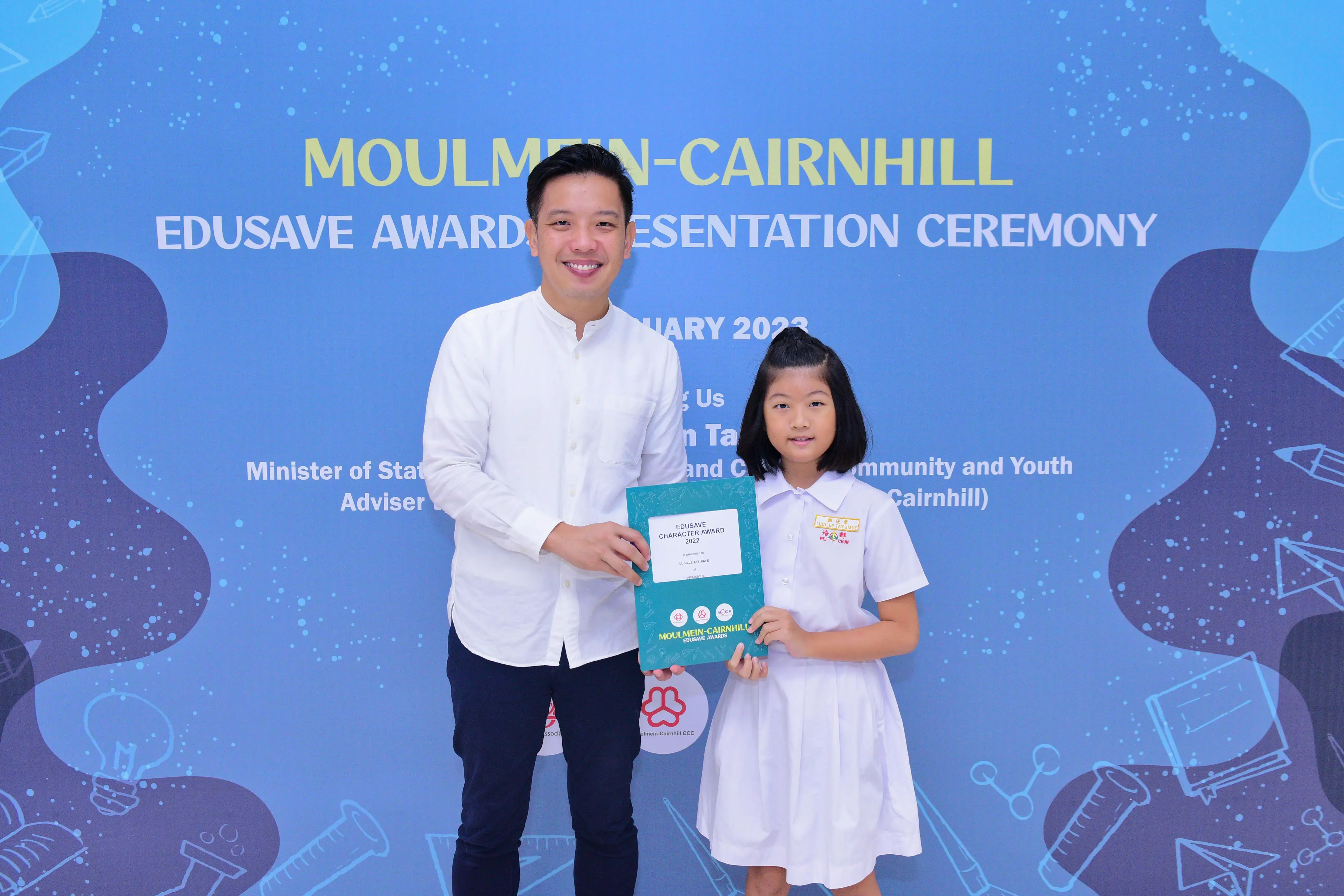 A man and a young girl hold an Edusave Character Award certificate at the Moulmein-Cairnhill Awards Ceremony 2023.
