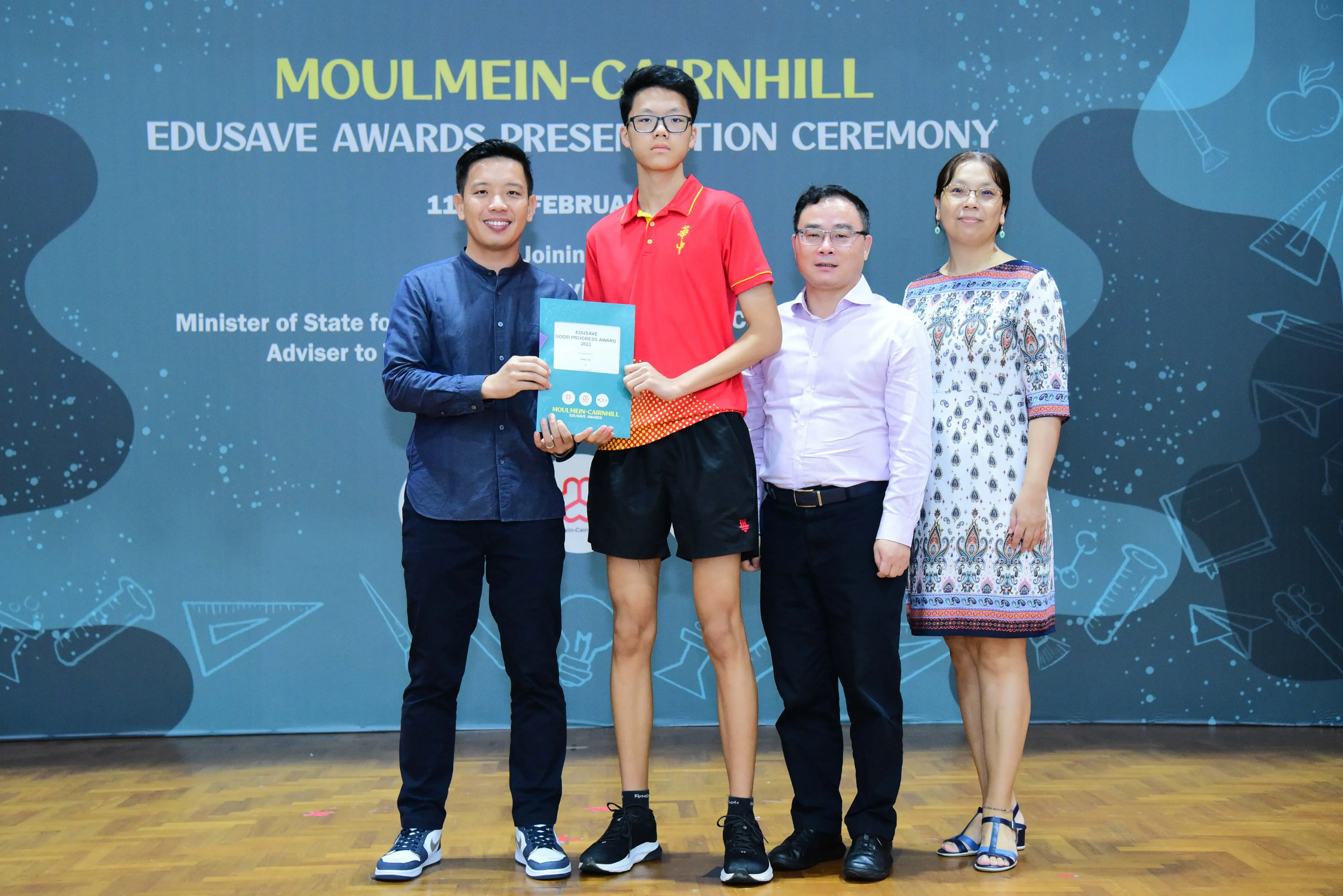 Four people pose at the Moulmein-Cairnhill Edusave Awards Presentation Ceremony, with a teen holding a certificate.