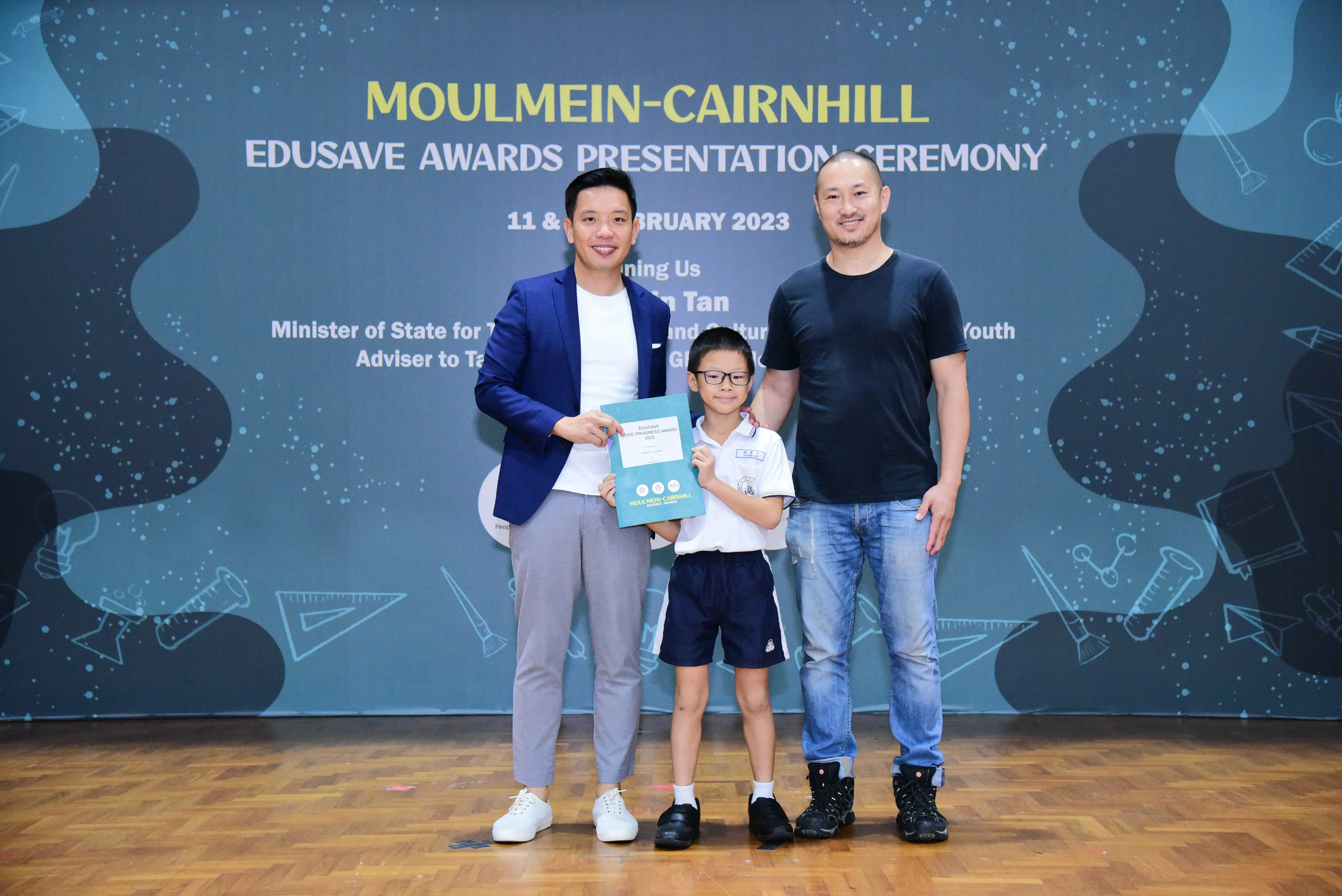 Two men and a young boy holding a certificate pose at the Moulmein-Cairnhill Edusave Awards Ceremony, February 2023.
