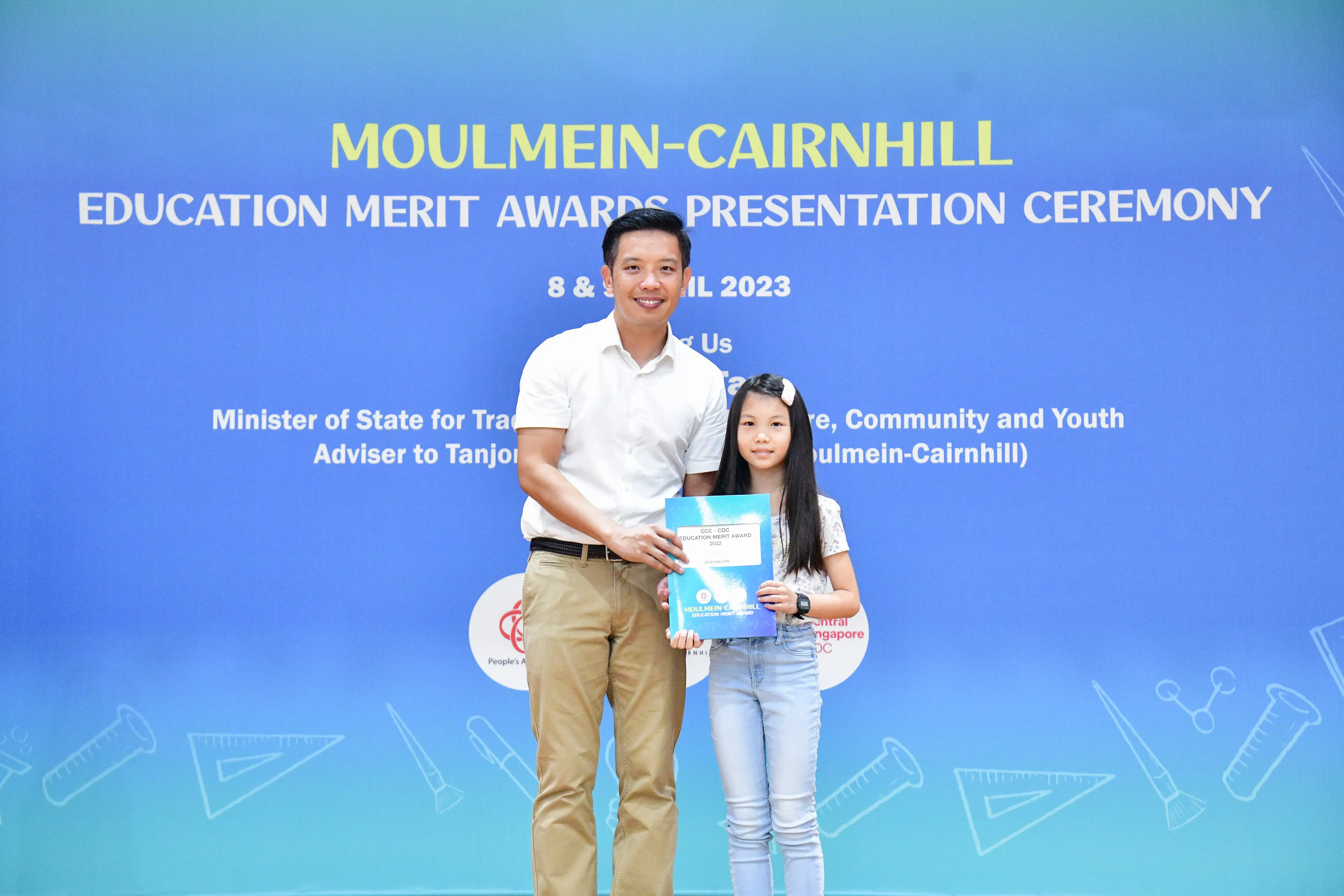 A man and a young girl hold a certificate together at the Moulmein-Cairnhill Education Merit Awards Ceremony 2023.