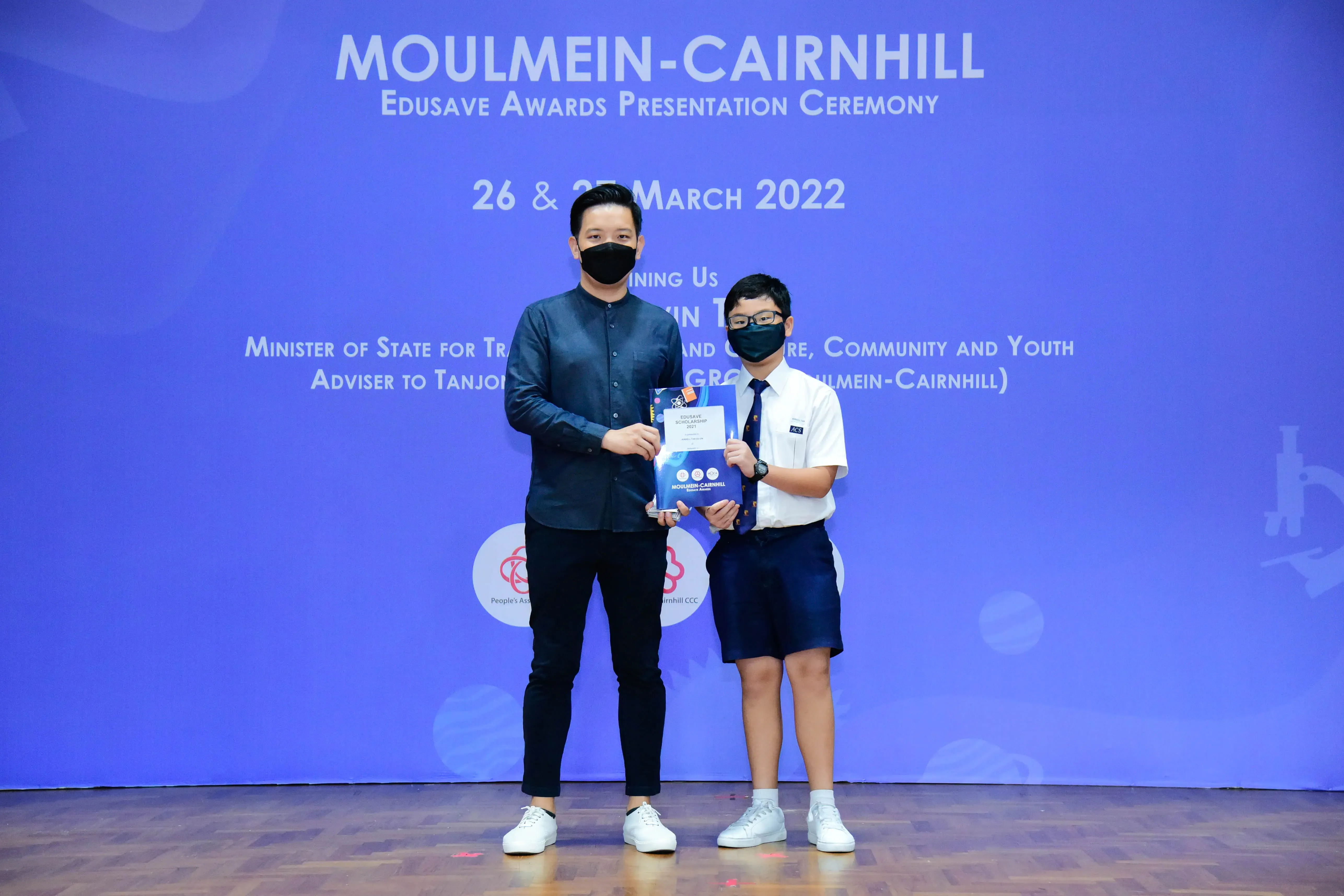 An adult and a uniformed student hold an award booklet at the Moulmein-Cairnhill Edusave Awards Ceremony, March 2022.