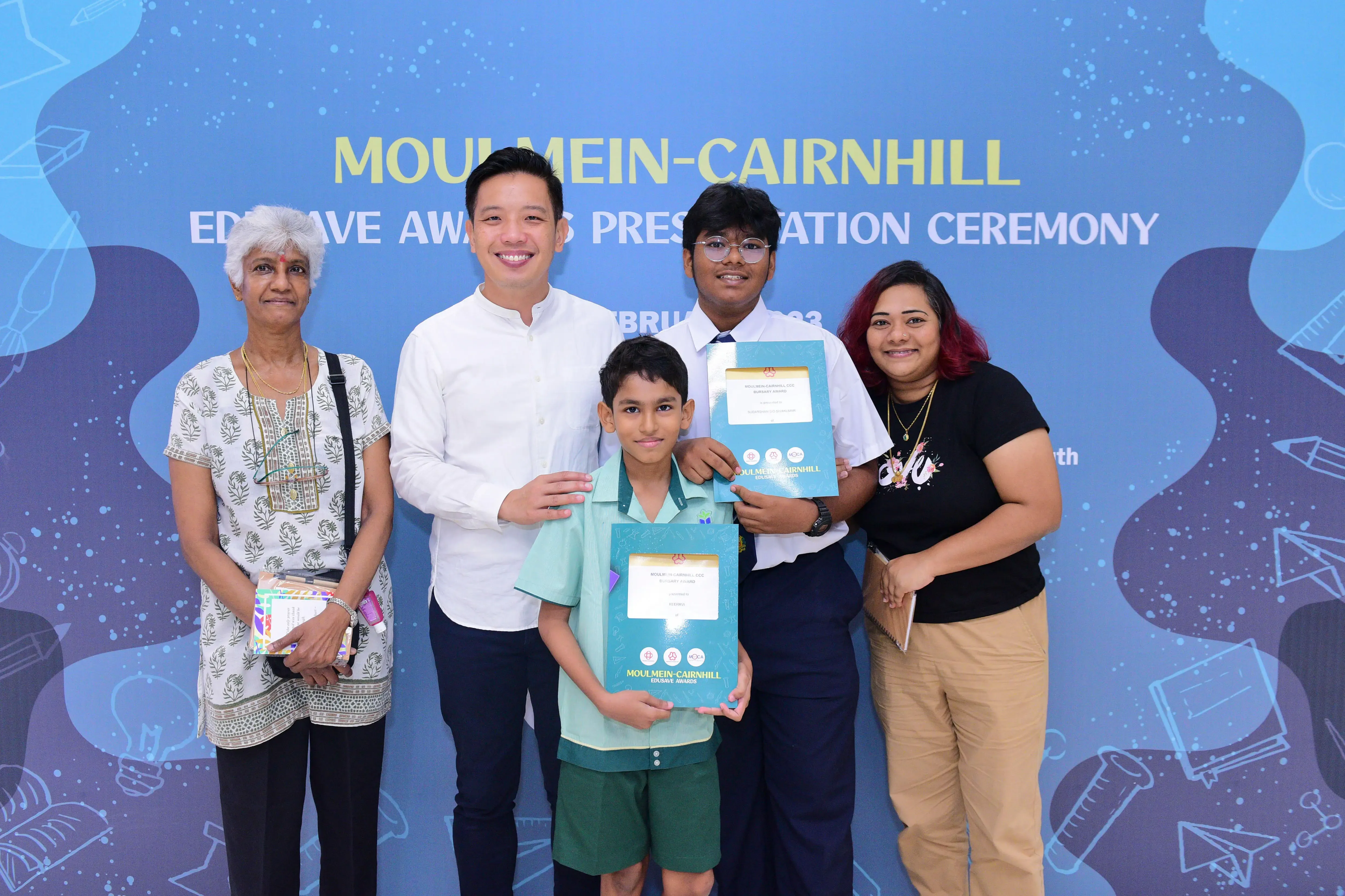 Five people pose at the Moulmein-Cairnhill Edusave Awards Presentation Ceremony, two boys holding award certificates.