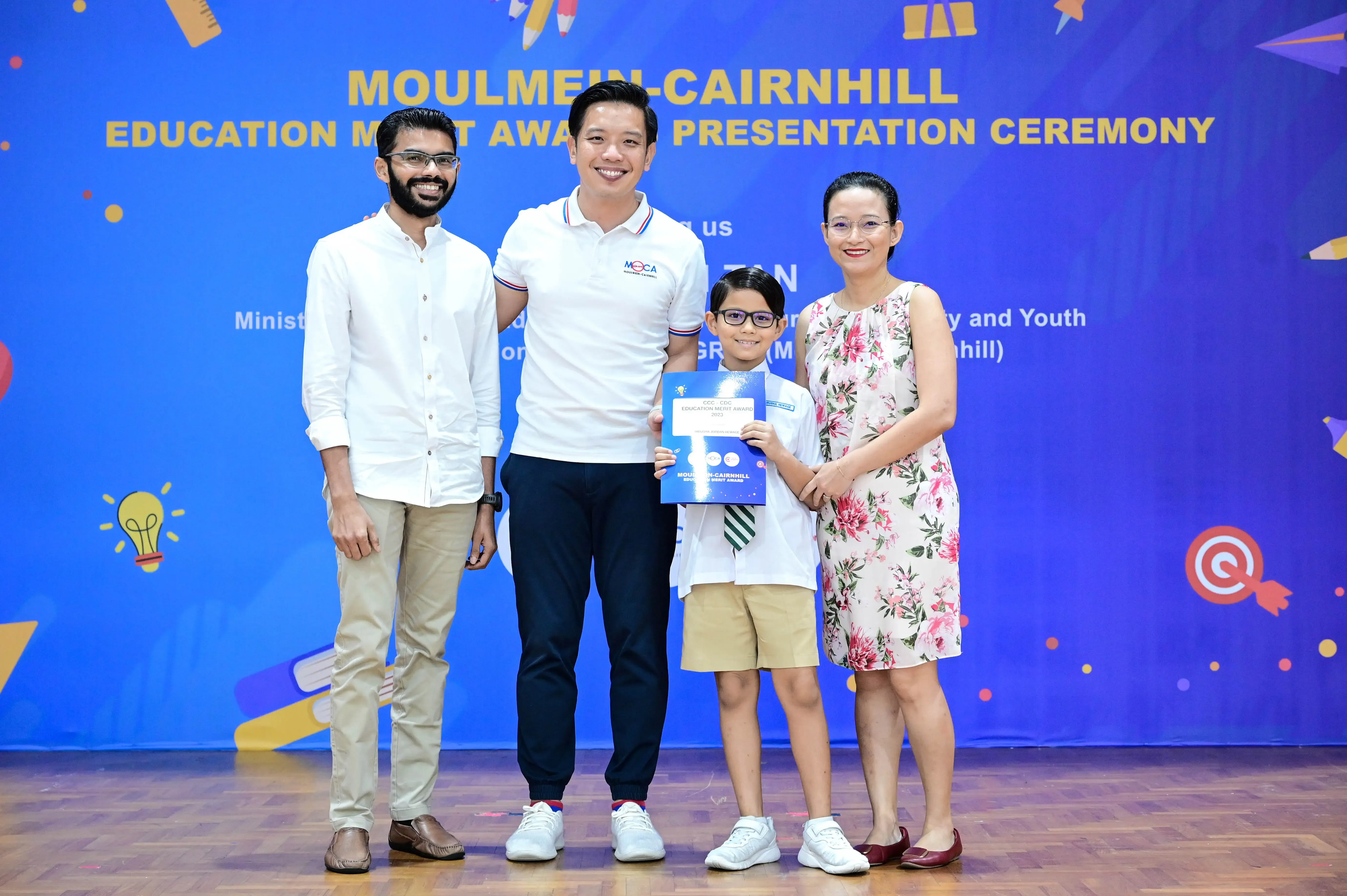 Four people pose at the Moulmein-Cairnhill Education Merit Award Presentation Ceremony, with a boy holding a certificate.