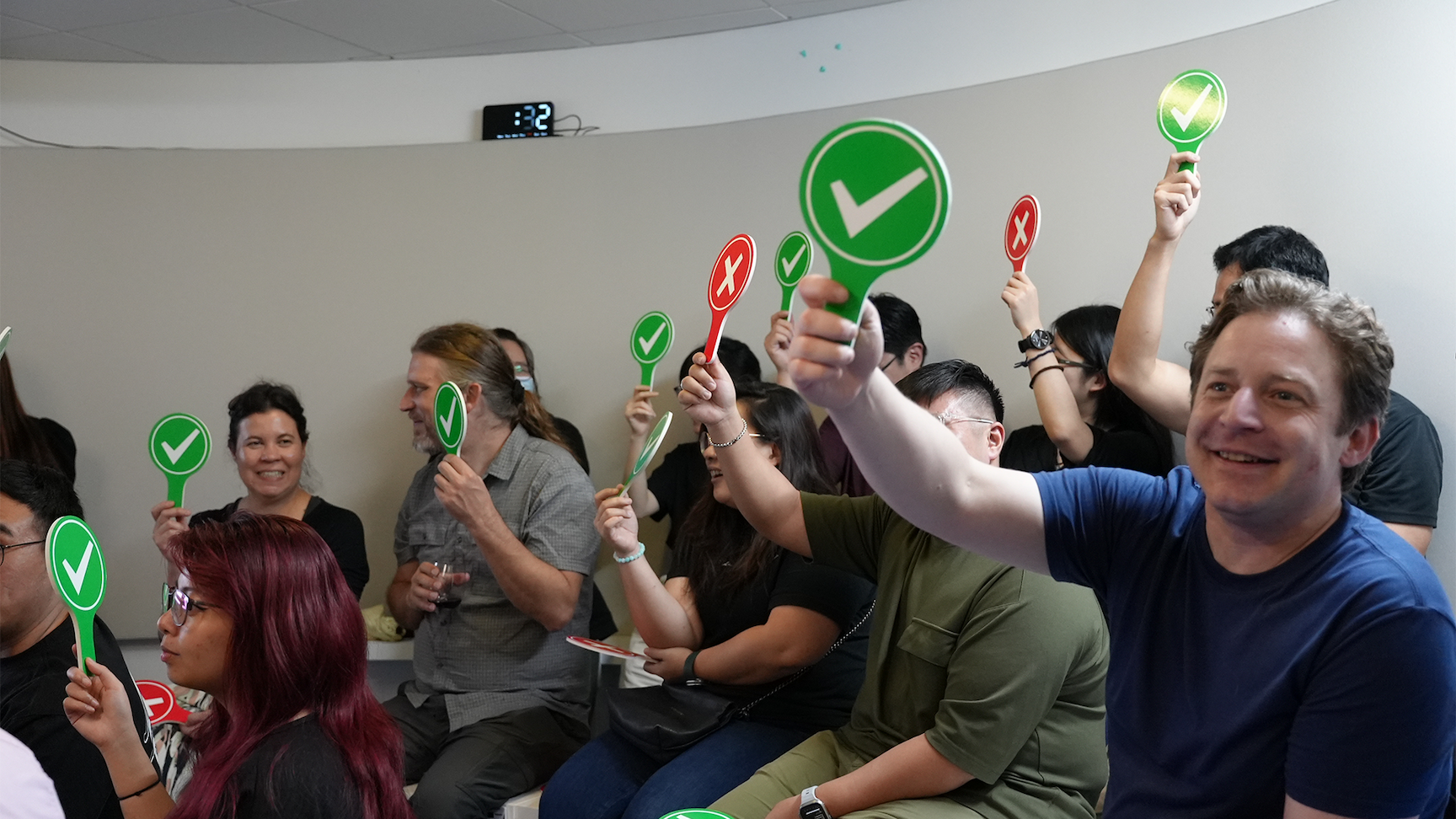 A group of people seated indoors holding up green checkmark and red X paddles during a voting activity.