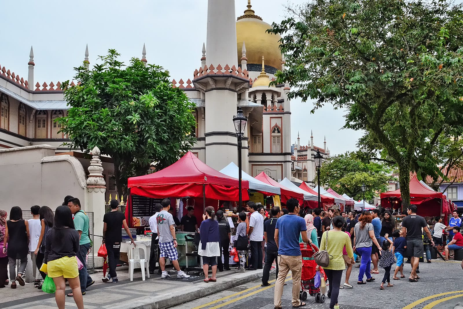 Crowded street market with red tents in front of a mosque with a large golden dome and tall minaret.