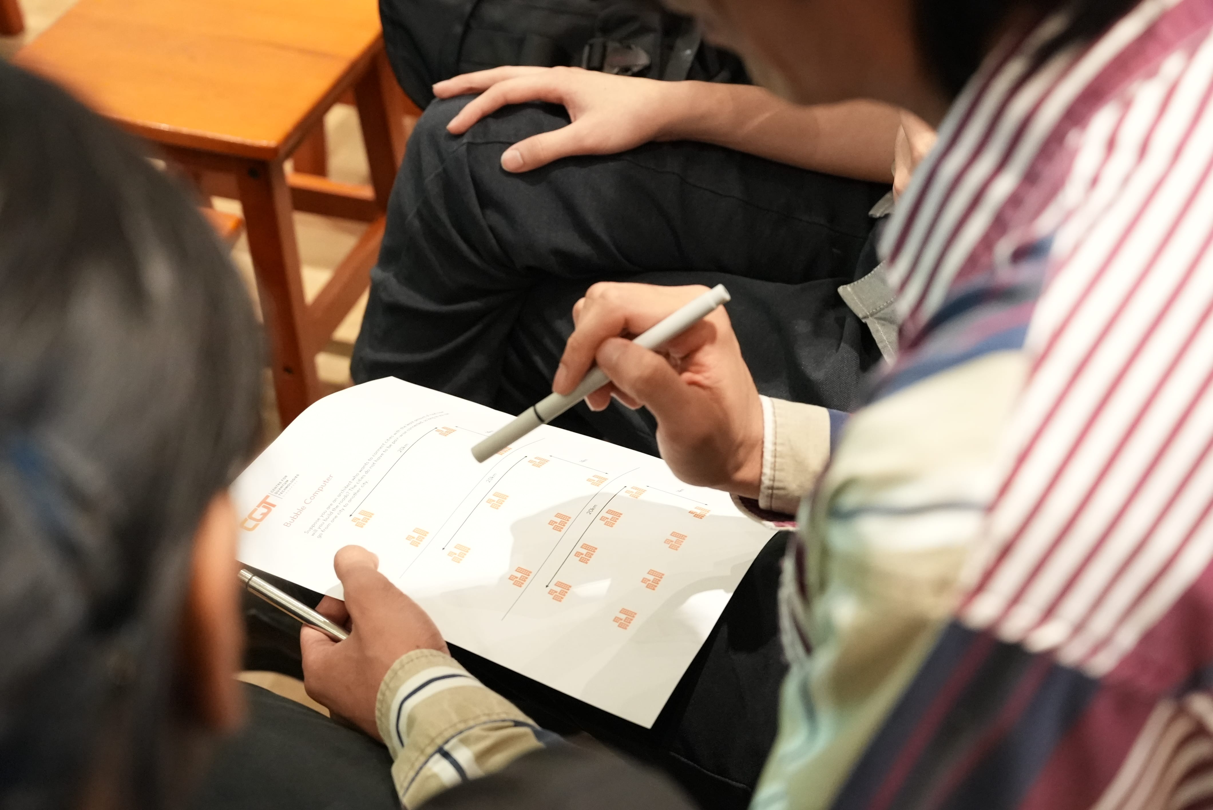 Two people holding pens review a printed document with orange text and charts during a meeting.