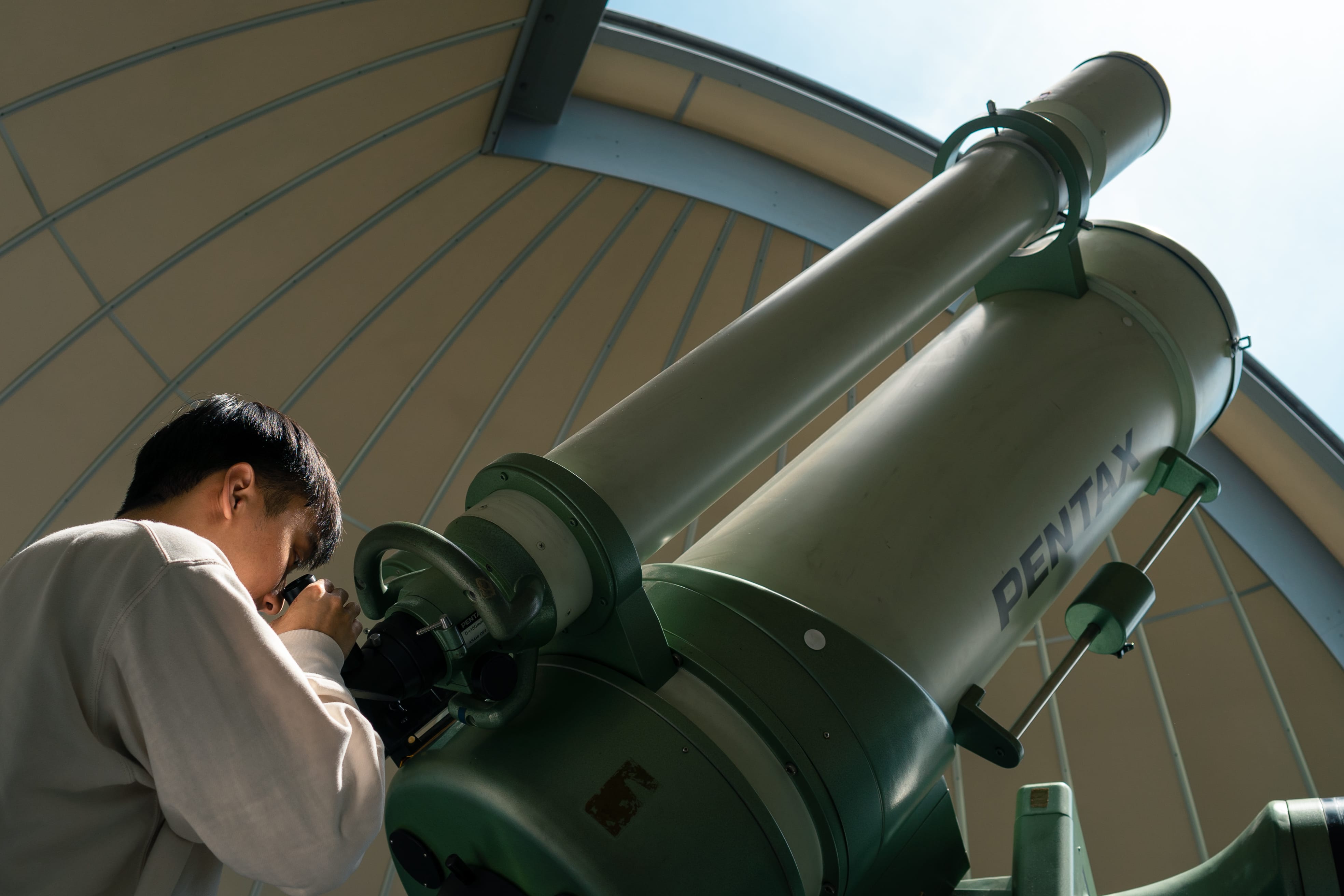 Jarrod Chua looks through the eyepiece of a large Pentax telescope inside a domed observatory.