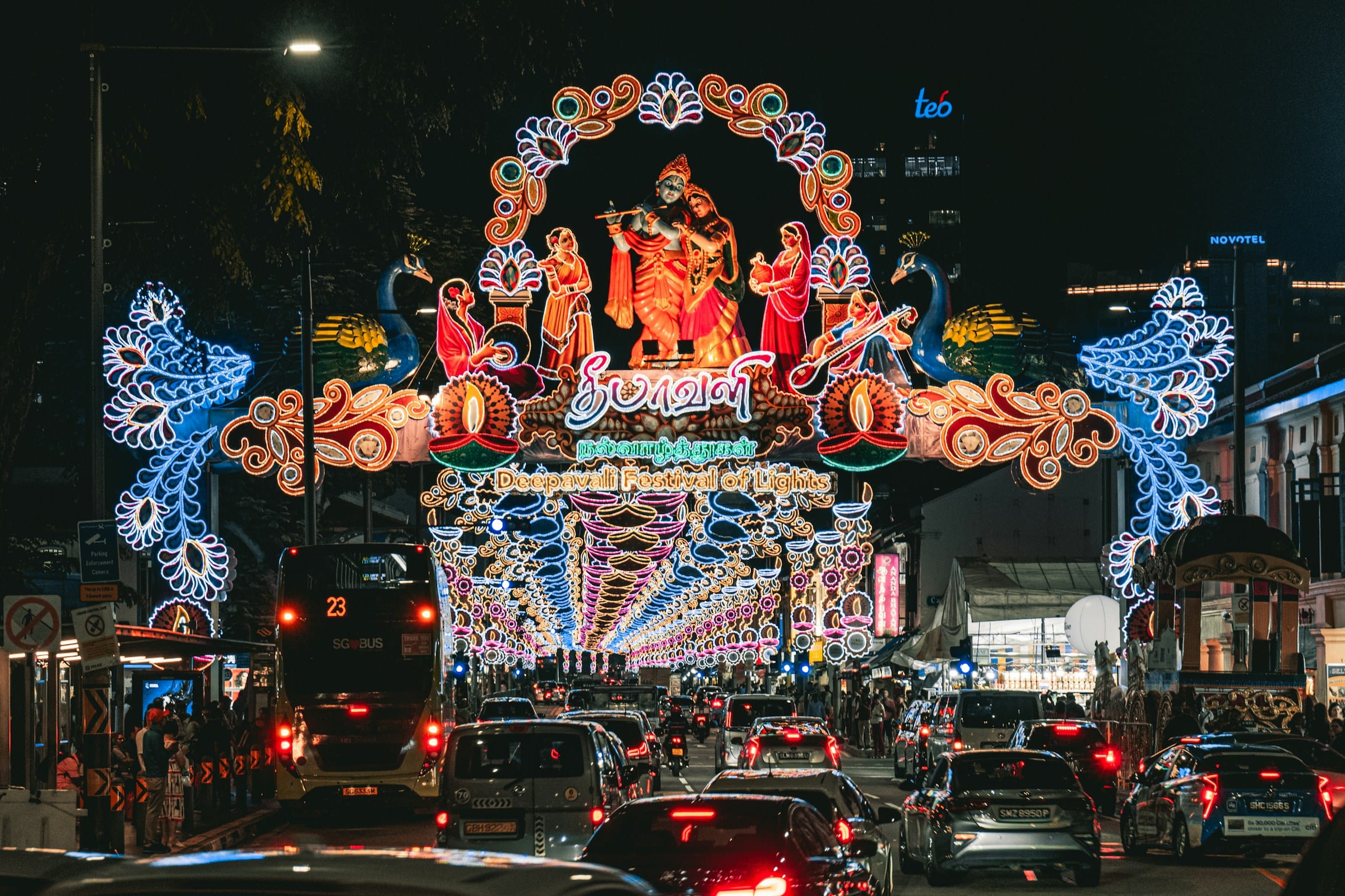 Colorful illuminated Deepavali Festival of Lights arch with Hindu deity figures over a busy night street.