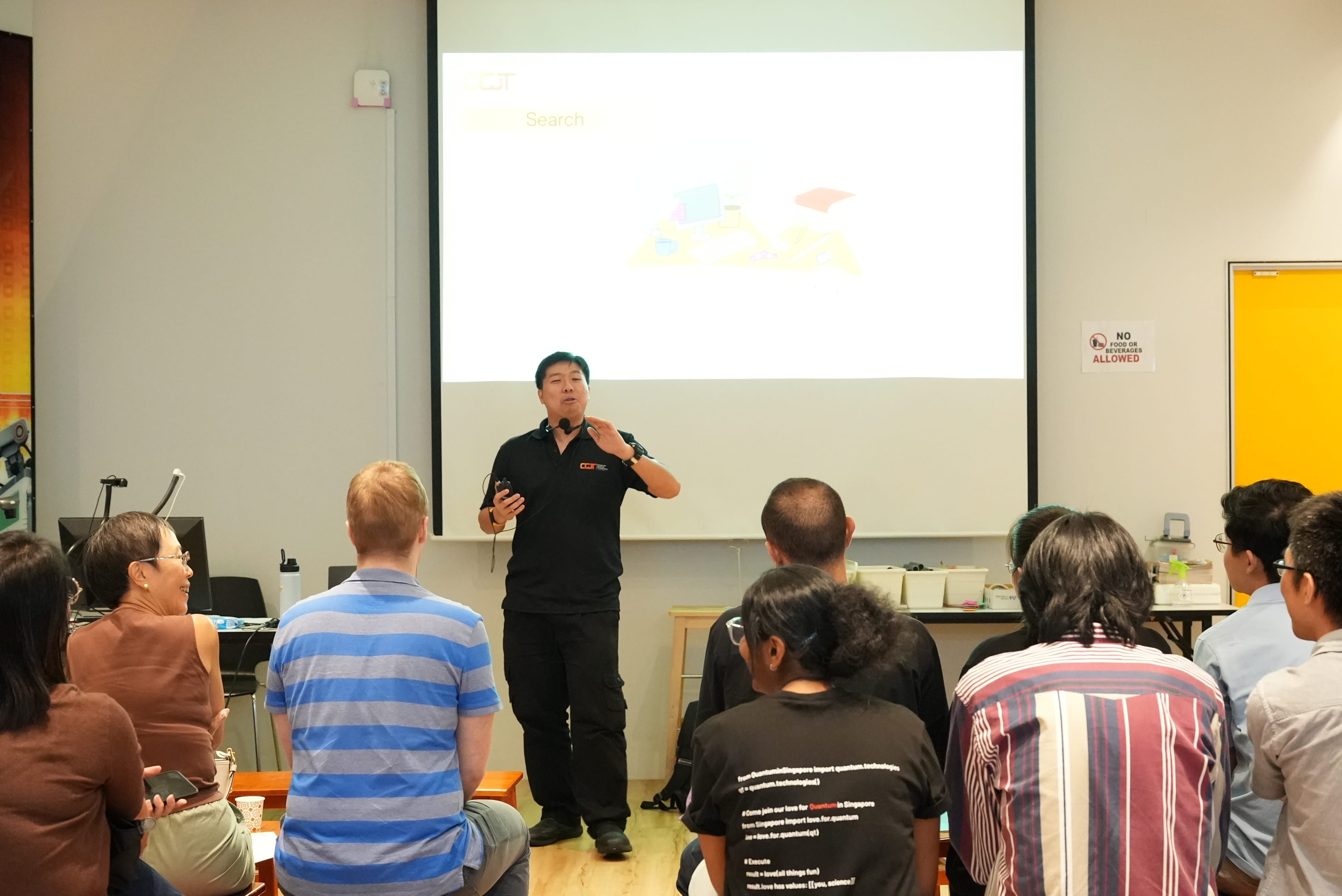 A man in a black shirt presents to a seated audience in front of a projected slide showing "Search."
